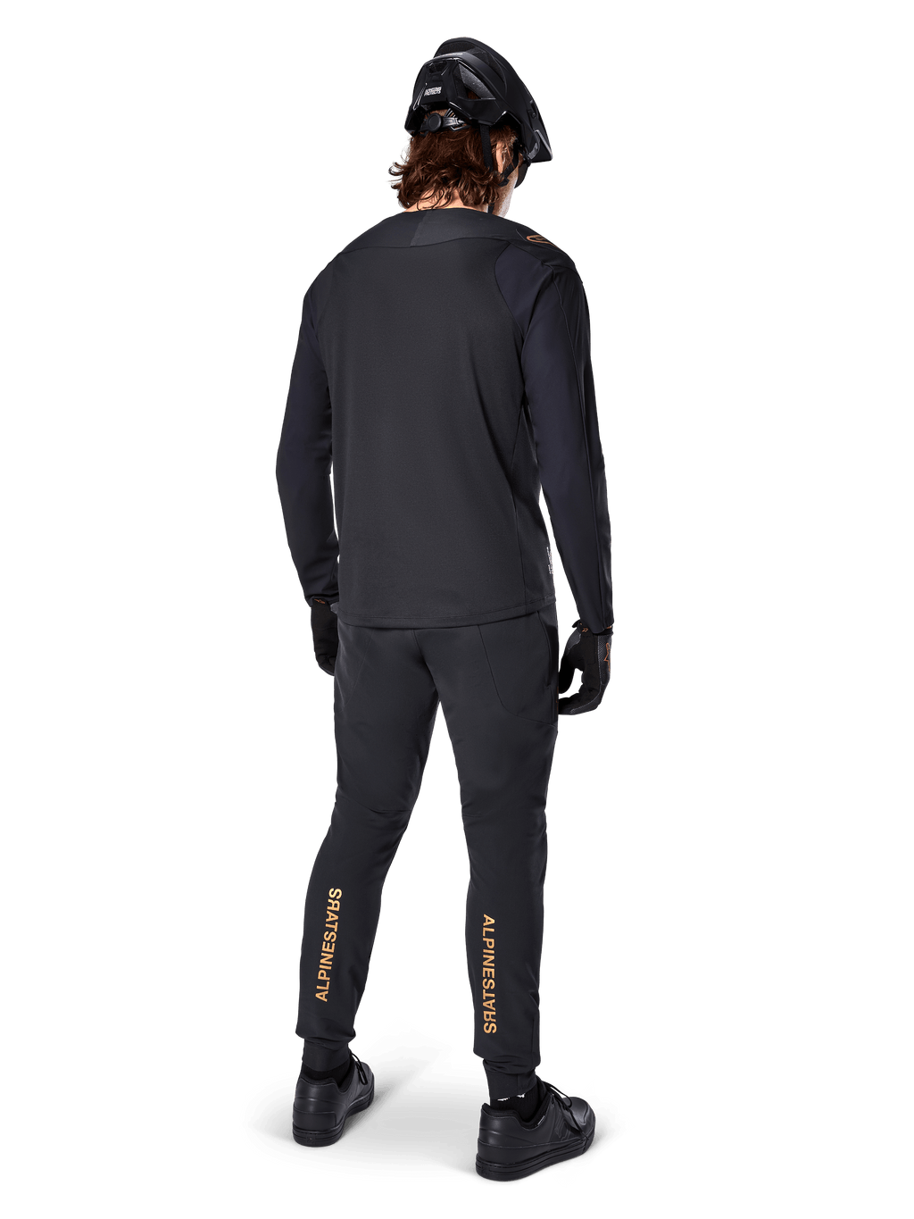 Vista traseira de um ciclista de BTT a usar a Jersey de Manga Longa Alpinestars A-Aria Polartec Switch em preto, combinada com calças de BTT pretas com o logótipo Alpinestars em bege na zona das gémeas, capacete e luvas pretos, equipamento de ciclismo profissional para trilhos.