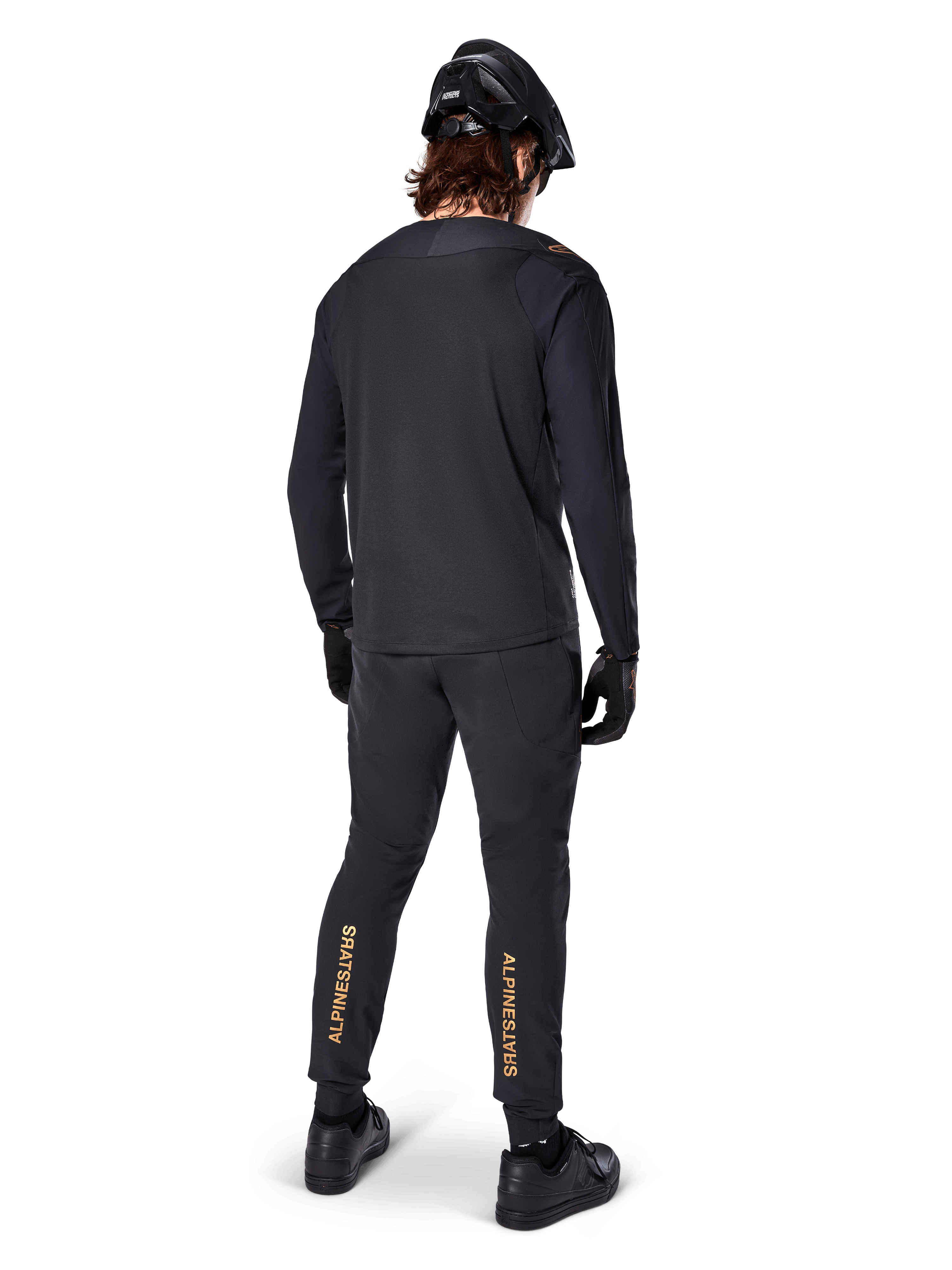 Vista traseira de um ciclista de BTT a usar a Jersey de Manga Longa Alpinestars A-Aria Polartec Switch em preto, combinada com calças de BTT pretas com o logótipo Alpinestars em bege na zona das gémeas, capacete e luvas pretos, equipamento de ciclismo profissional para trilhos.