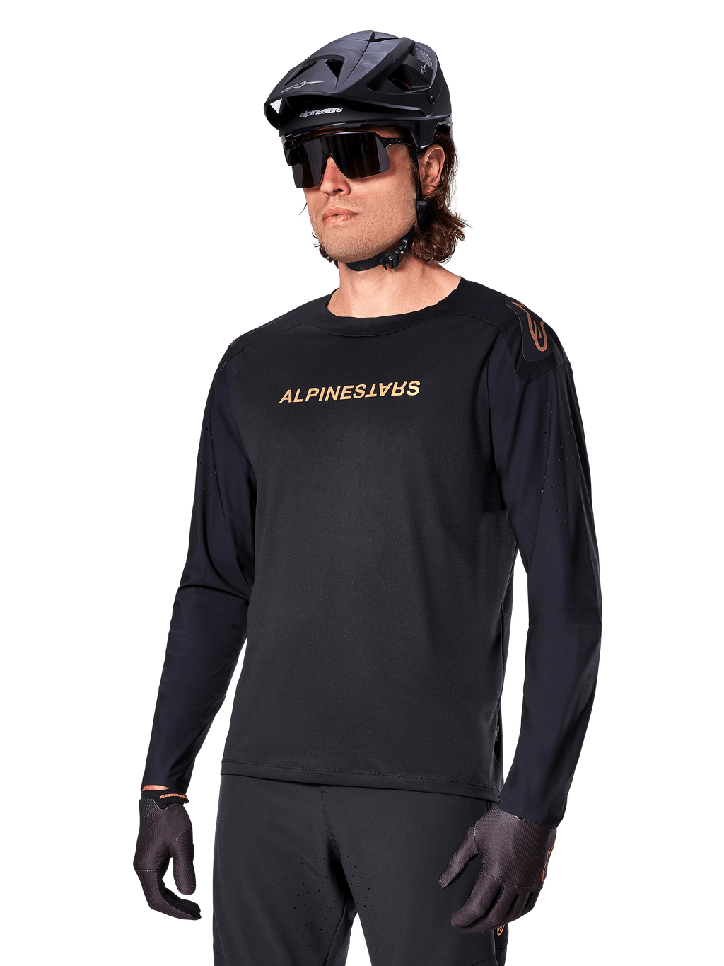 Jersey de manga comprida Alpinestars A-Aria Polartec Switch, preto com logótipo dourado, vestuário de BTT para ciclismo de montanha, usado com capacete preto e óculos de sol, com ventilação cortada a laser nas mangas e tecido Polartec com absorção de humidade para desempenho em todo-o-terreno