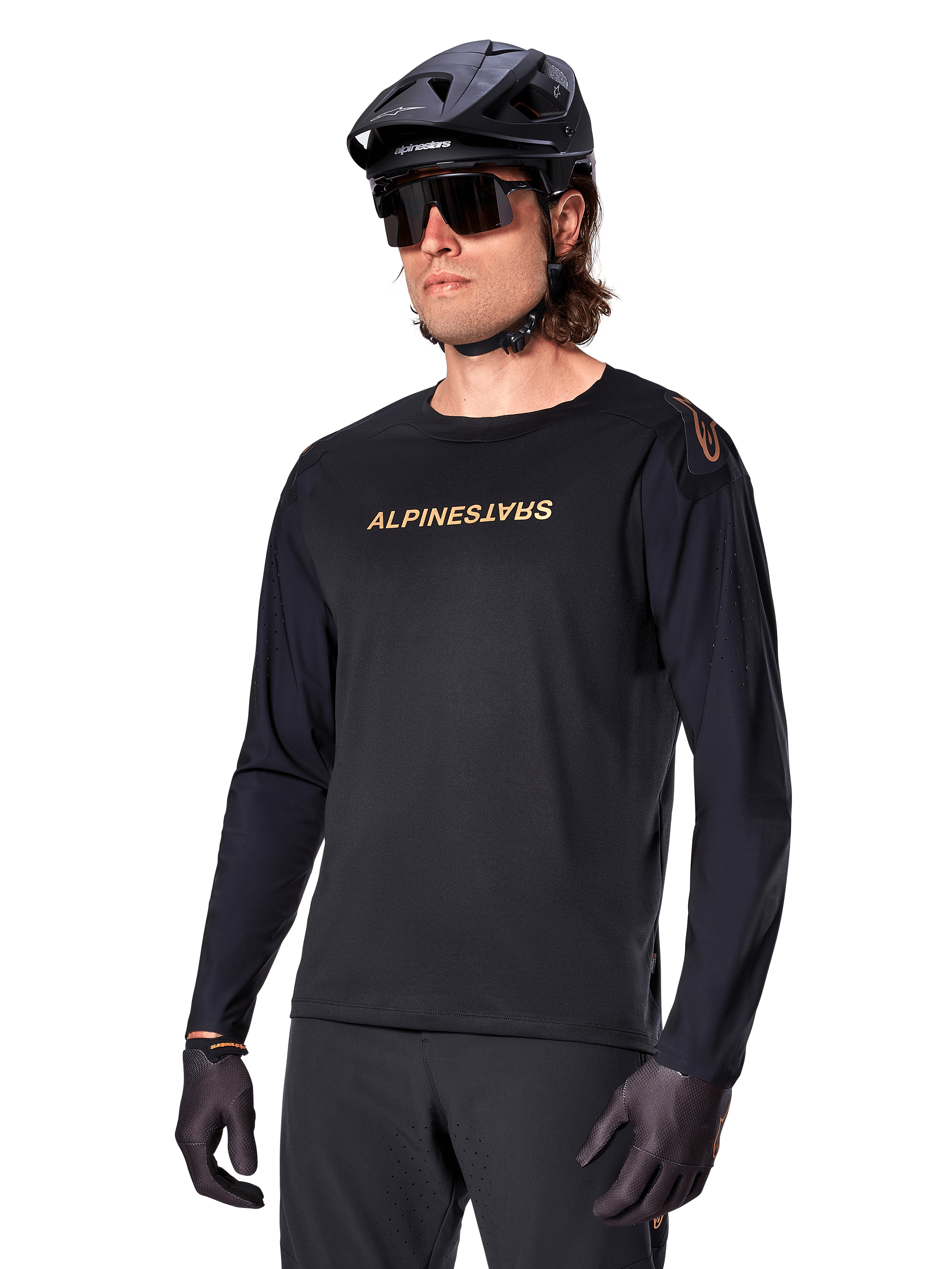 Jersey de manga comprida Alpinestars A-Aria Polartec Switch, preto com logótipo dourado, vestuário de BTT para ciclismo de montanha, usado com capacete preto e óculos de sol, com ventilação cortada a laser nas mangas e tecido Polartec com absorção de humidade para desempenho em todo-o-terreno
