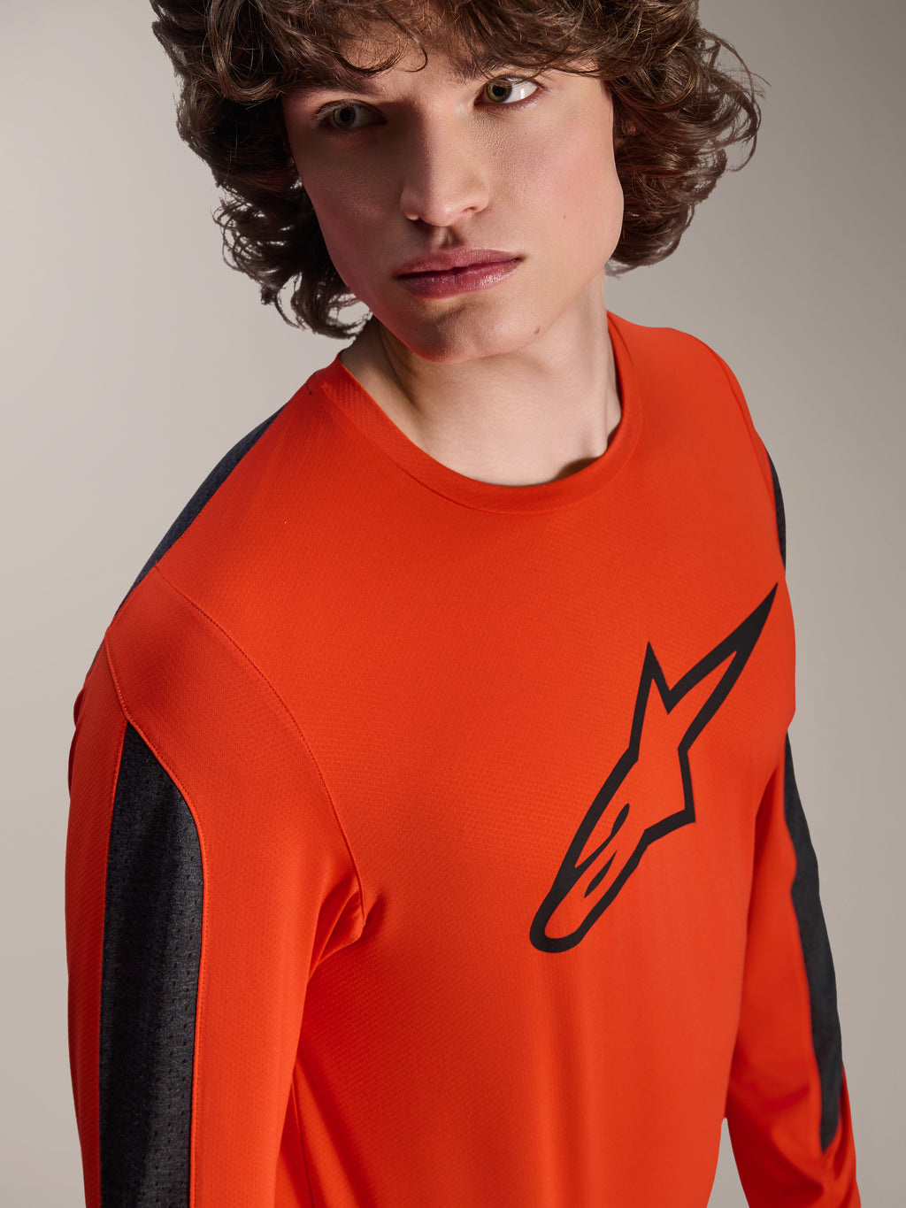 Camisola de Manga Comprida Alpinestars A-Dura Insert Astar, camisola de MTB cor Spicy Orange com logótipo Astar grande em preto no peito, painéis das mangas em cinzento escuro, vestida por um modelo num grande plano de estúdio, tecido técnico texturizado.