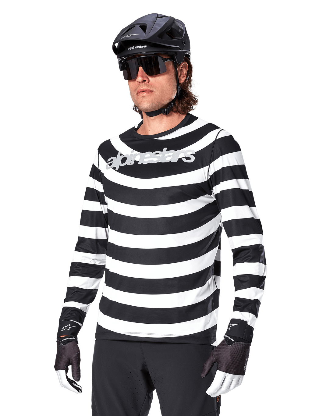 Camisola de Manga Comprida Alpinestars A-Aria Oscar, camisola de ciclismo BTT, riscas horizontais pretas e brancas, usada com capacete preto e óculos de sol, com logótipo Alpinestars no peito, vestuário de performance para BTT