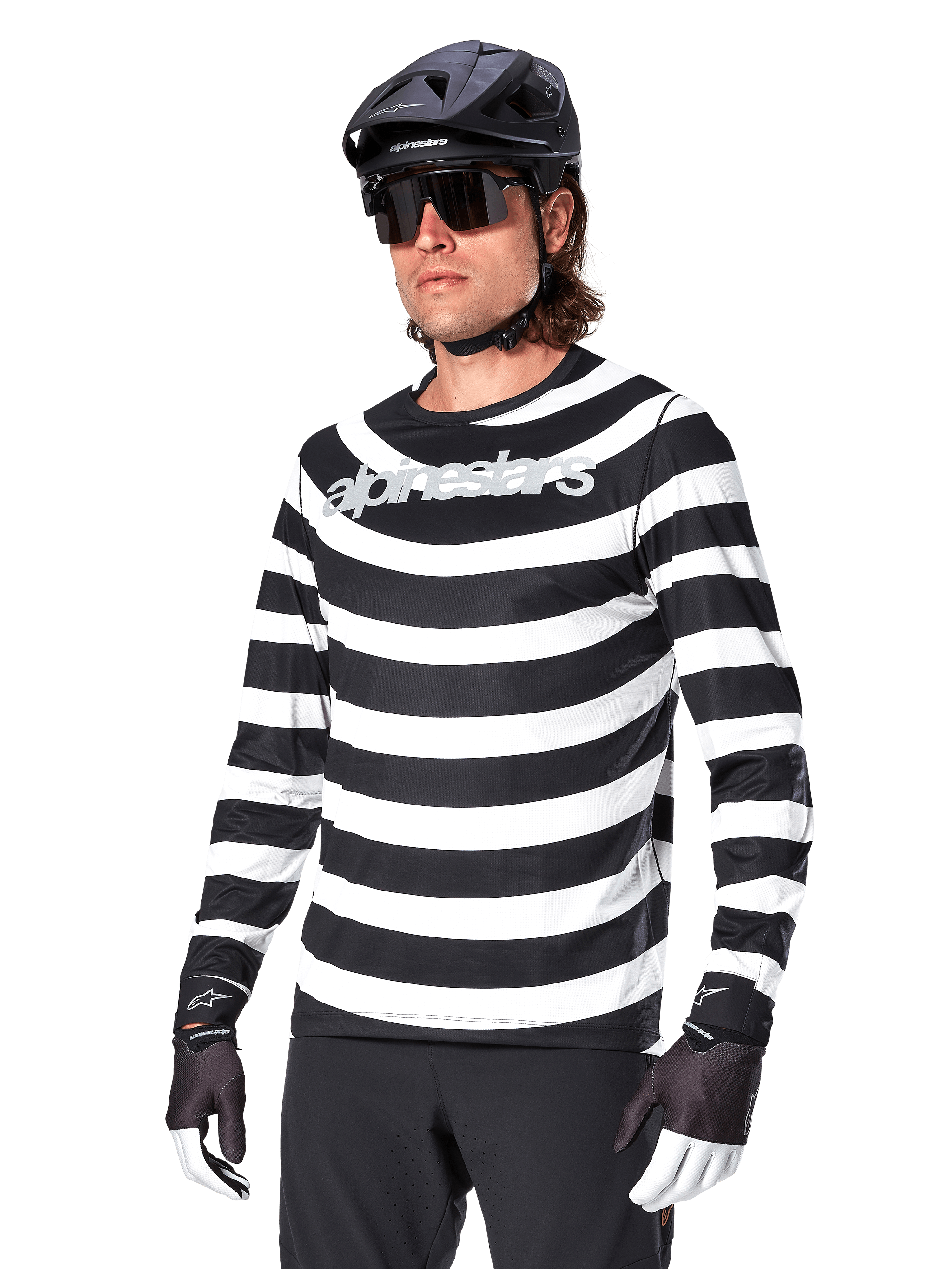 Camisola de Manga Comprida Alpinestars A-Aria Oscar, camisola de ciclismo BTT, riscas horizontais pretas e brancas, usada com capacete preto e óculos de sol, com logótipo Alpinestars no peito, vestuário de performance para BTT