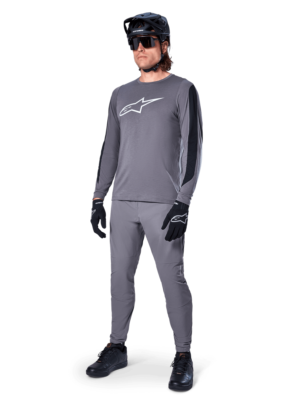 Alpinestars A-Dura Dri Astar Jersey, Long Sleeve MTB Jersey, Dark Gray with white chest logo, black mesh panels on sleeves, worn with matching gray pants, black helmet, and gloves, performance mountain bike apparel