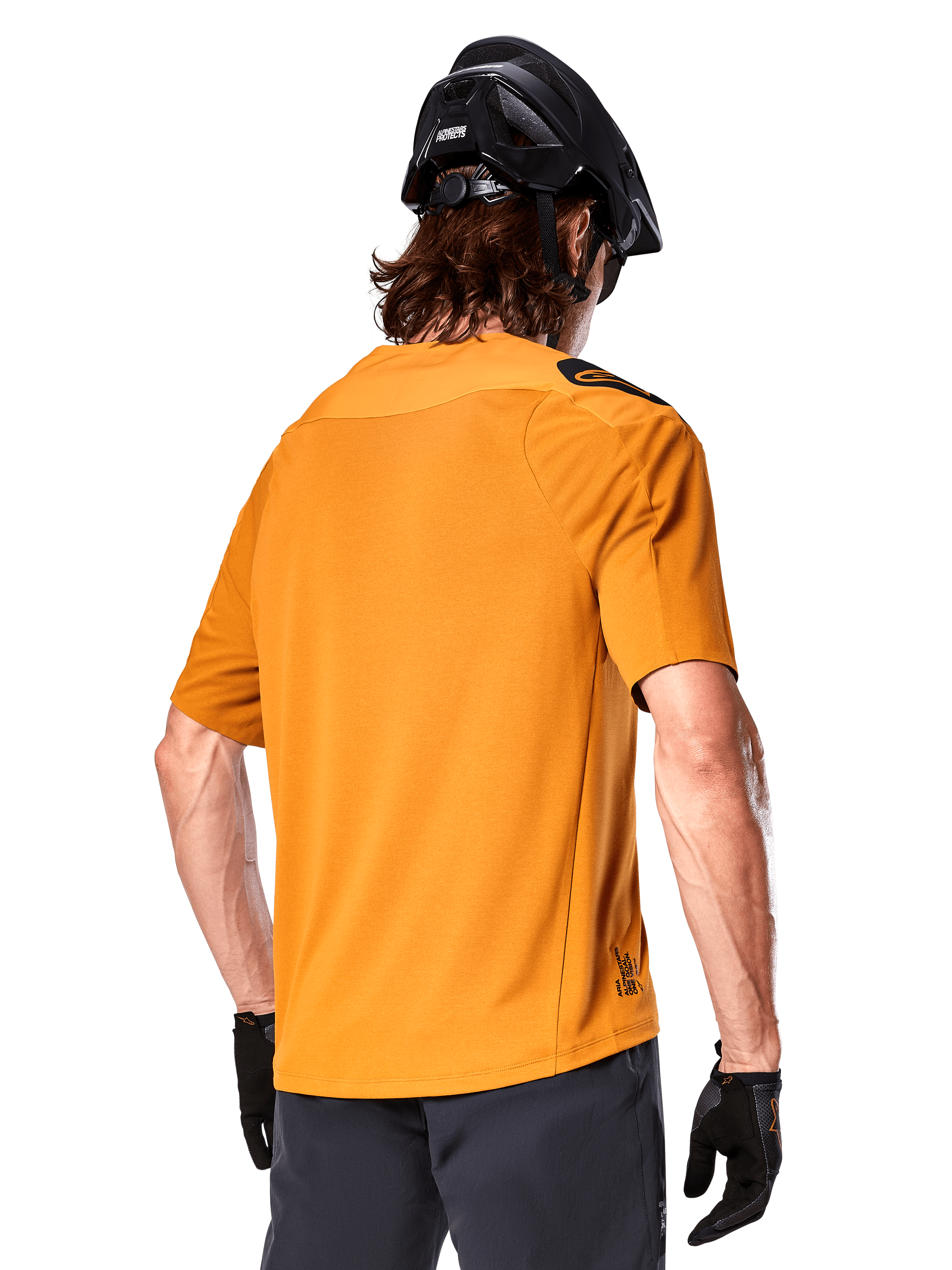 Camisola Alpinestars A-Aria Polartec Switch, camisola de MTB de manga curta, Dark Gold, vista traseira que mostra o ajuste de desempenho, usada com capacete preto e calções cinzentos, vestuário de trilhos durável e respirável