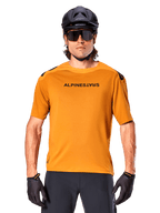 Alpinestars A-Aria Polartec Switch Jersey - Manga Curta, Dourado Escuro, ciclista de BTT a usar capacete preto e óculos de sol, vestuário de ciclismo de performance para trilhos de BTT