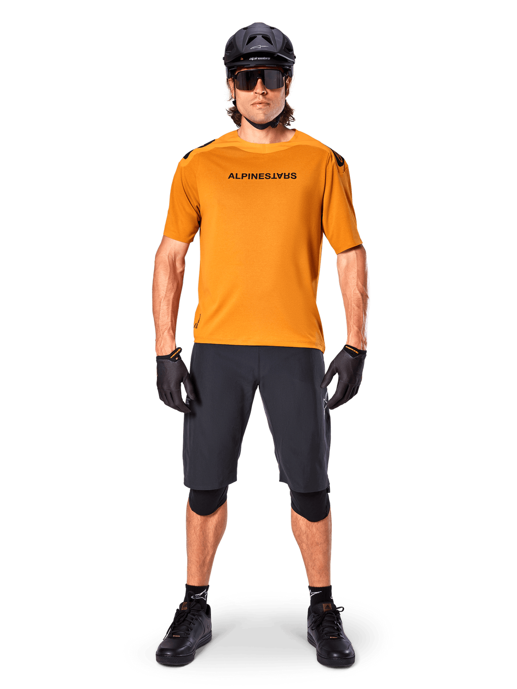 Ciclista masculino a usar a camisola de manga curta Alpinestars A-Aria Polartec Switch em Dark Gold, combinada com calções de BTT pretos, capacete, óculos de sol e luvas, equipamento profissional para trilhos de BTT