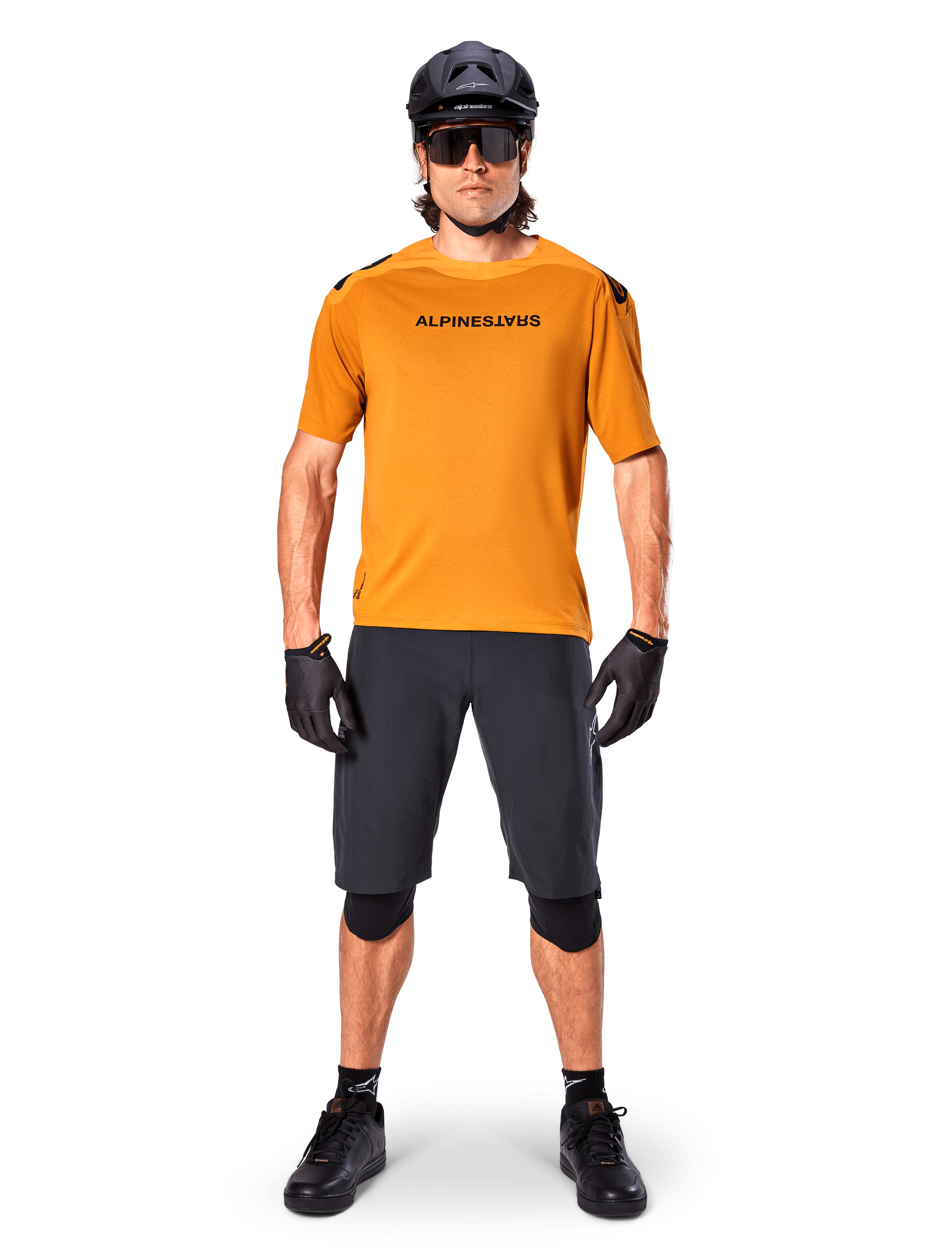 Ciclista masculino a usar a camisola de manga curta Alpinestars A-Aria Polartec Switch em Dark Gold, combinada com calções de BTT pretos, capacete, óculos de sol e luvas, equipamento profissional para trilhos de BTT