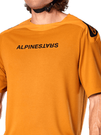 Alpinestars A-Aria Polartec Switch Jersey, camisola de manga curta para BTT, cor ouro escuro, com logótipo Alpinestars preto espelhado no peito, tecido de desempenho técnico para a prática de trilhos de BTT