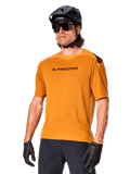 Alpinestars A-Aria Polartec Switch Jersey, camisola de BTT de manga curta, Dark Gold com logótipo preto, usada por um modelo com capacete preto, óculos de sol e luvas de ciclismo, vestuário de BTT de alta performance