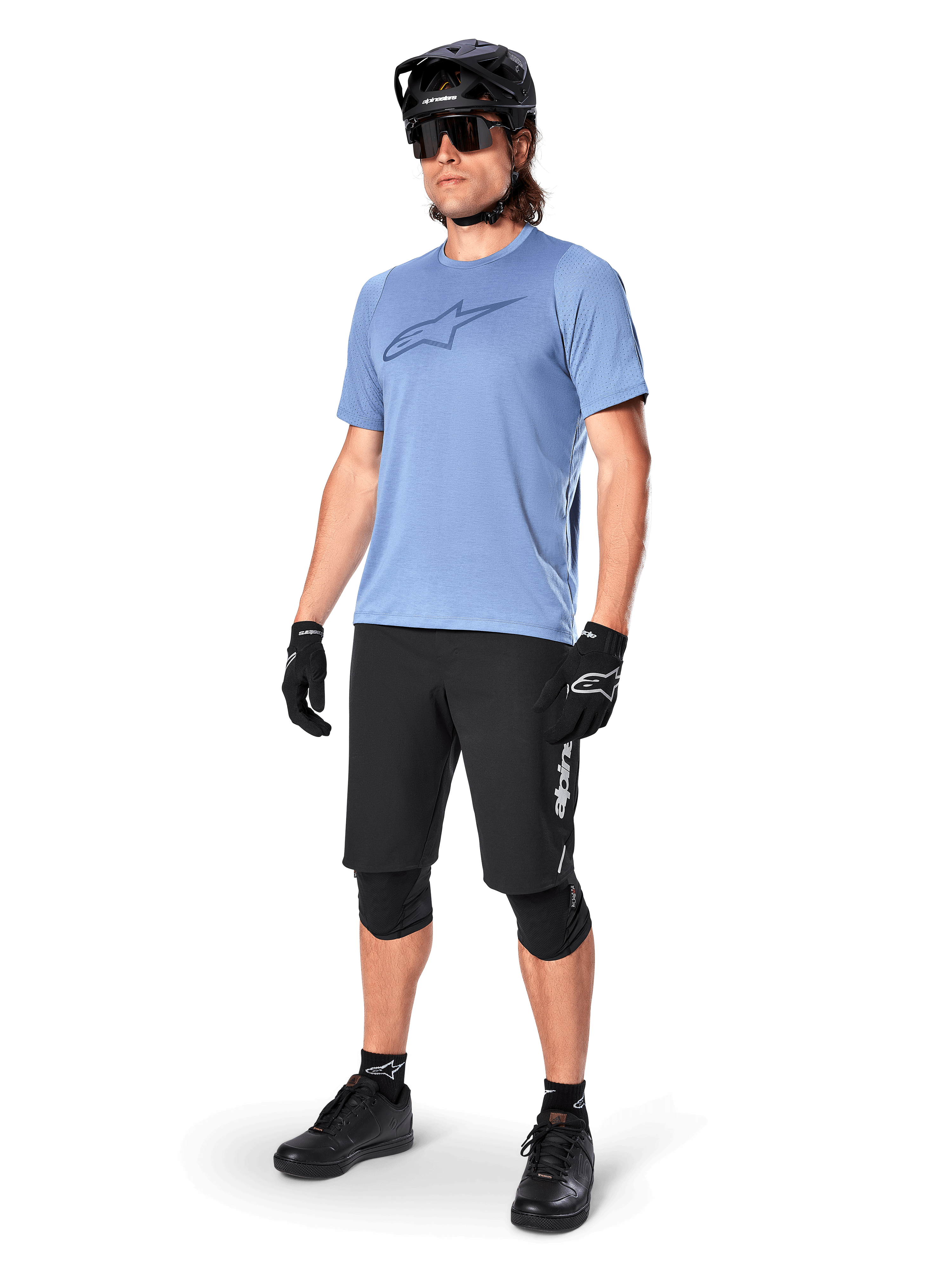 Male rider wearing the Alpinestars A-Dura Dri Astar Short Sleeve Jersey in Infinity Blue, paired with black MTB shorts, black helmet, sunglasses, knee pads, and gloves, complete mountain biking outfit