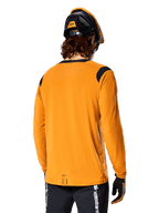 Camisola de Manga Comprida Alpinestars A-Dura Dri Wool em Dark Gold, vista traseira de um ciclista com capacete de BTT e luvas, apresentando painéis de malha pretos nos ombros e uma cauda mais longa, vestuário técnico de ciclismo para trilhos