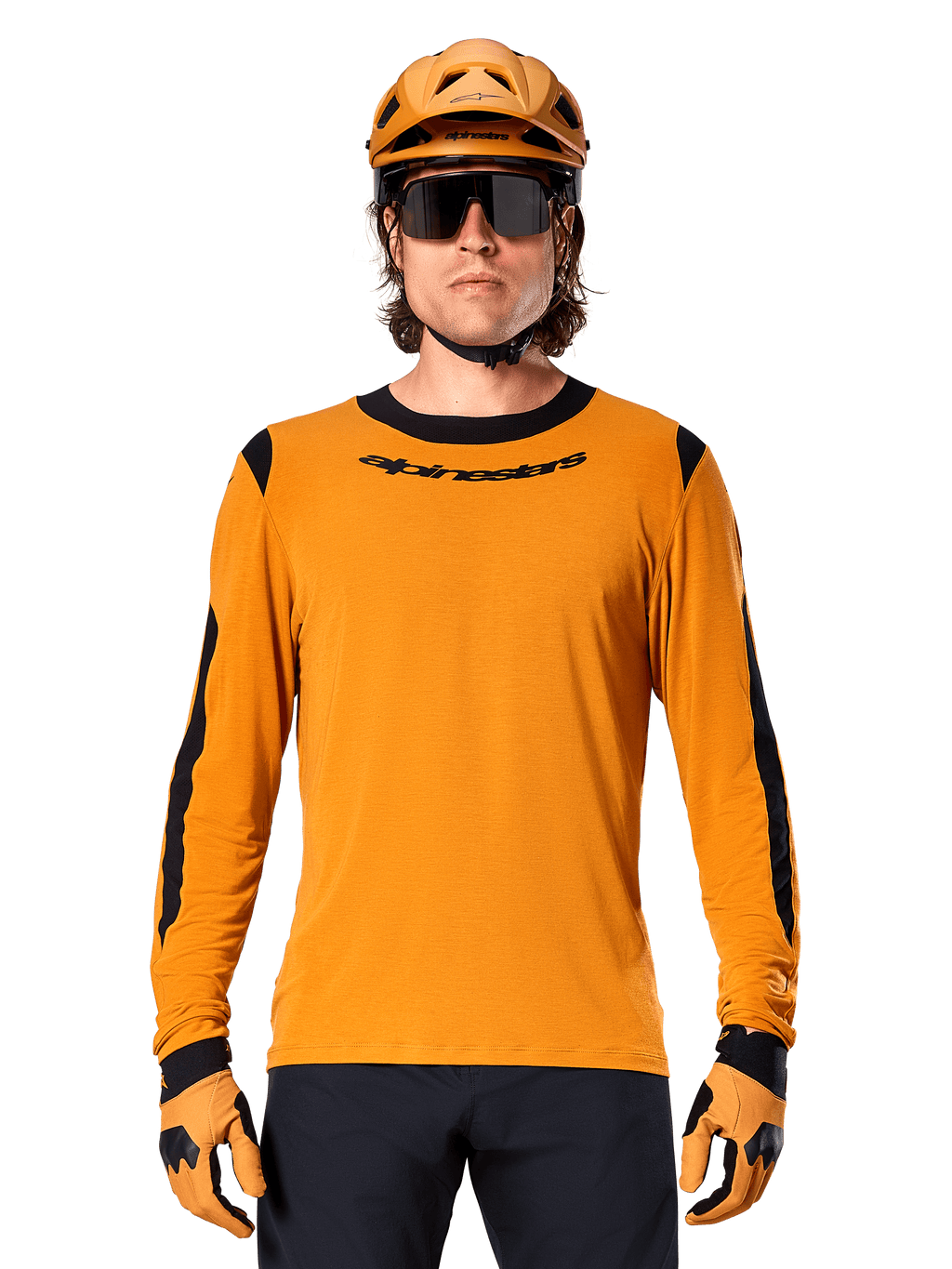 Modelo masculino a usar a camisola de manga comprida Alpinestars A-Dura Dri Wool em Dark Gold, coordenada com um capacete de BTT e luvas em dourado a condizer, painéis de malha pretos nos ombros e mangas, logótipo Alpinestars preto no peito, óculos de sol e calças escuras, vestuário técnico de BTT
