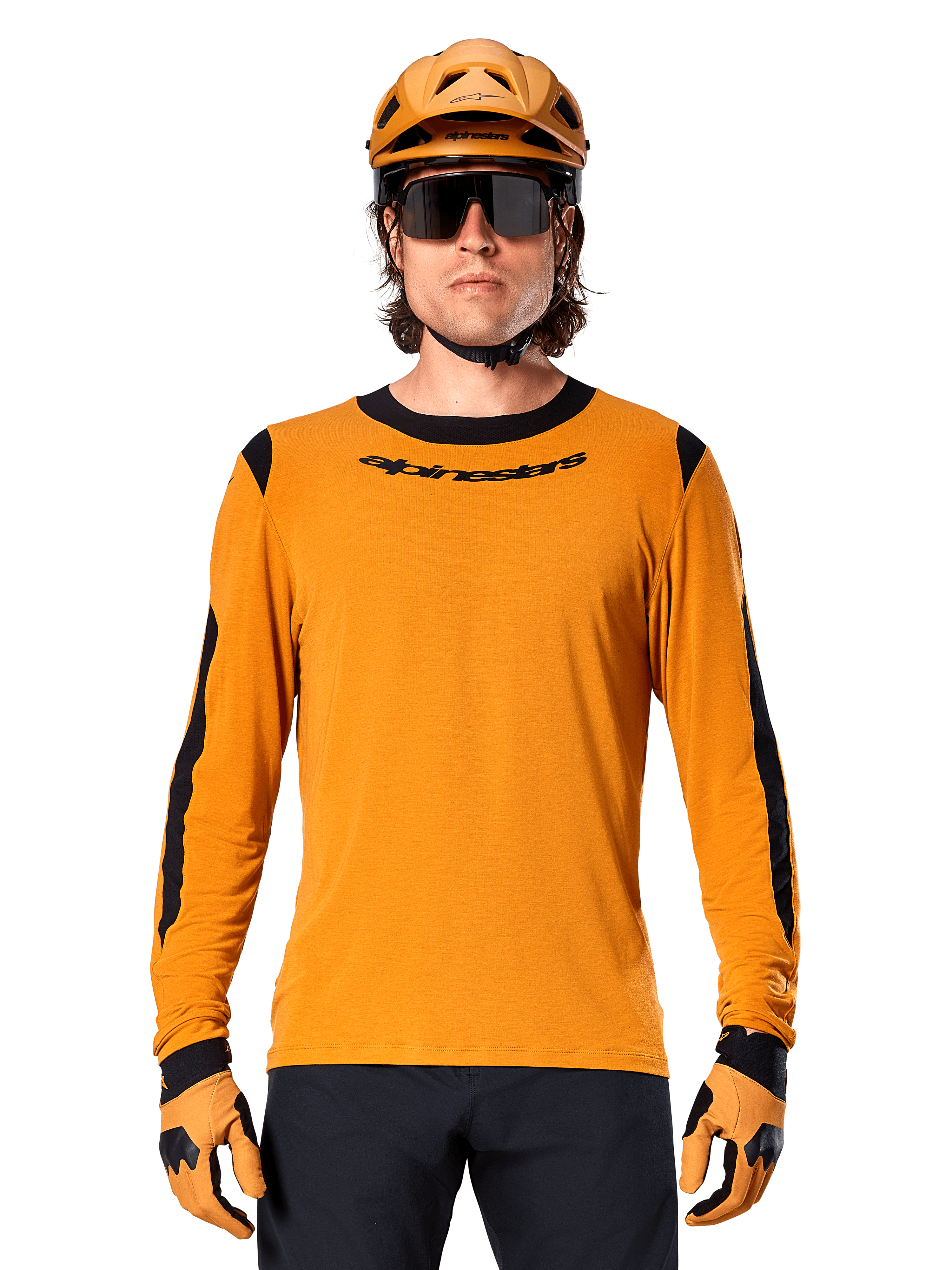 Modelo masculino a usar a camisola de manga comprida Alpinestars A-Dura Dri Wool em Dark Gold, coordenada com um capacete de BTT e luvas em dourado a condizer, painéis de malha pretos nos ombros e mangas, logótipo Alpinestars preto no peito, óculos de sol e calças escuras, vestuário técnico de BTT