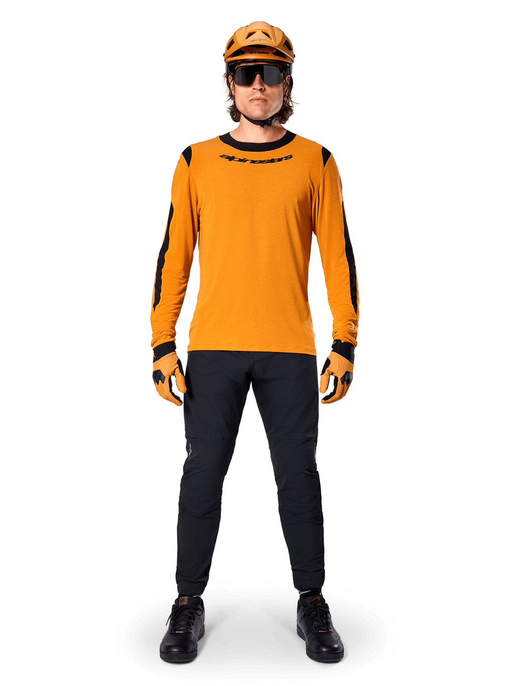 Ciclista de BTT com a Camisola de Manga Comprida Alpinestars A-Dura Dri Wool, Dark Gold com detalhes pretos no colarinho e nas mangas, combinada com calças pretas, capacete e luvas douradas a condizer e óculos de sol pretos, equipamento profissional de BTT