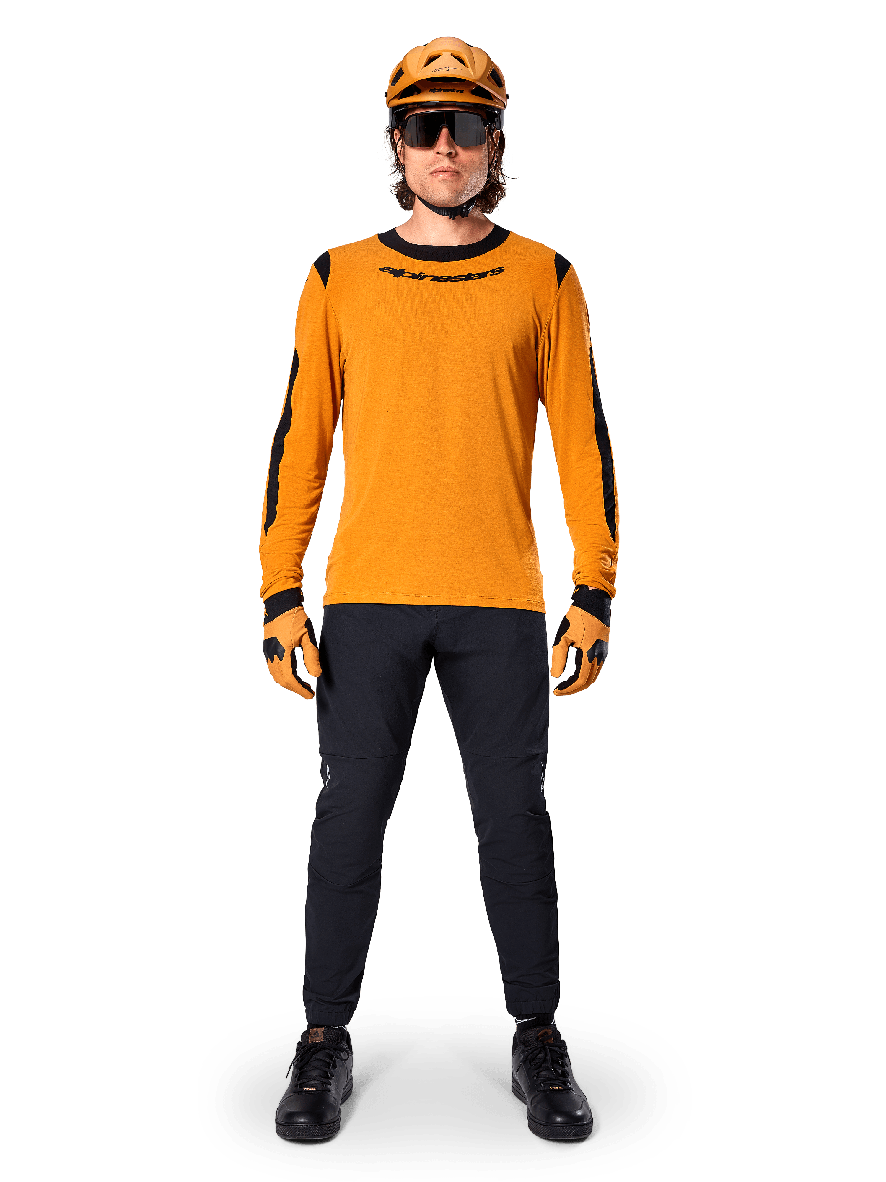 Ciclista de BTT com a Camisola de Manga Comprida Alpinestars A-Dura Dri Wool, Dark Gold com detalhes pretos no colarinho e nas mangas, combinada com calças pretas, capacete e luvas douradas a condizer e óculos de sol pretos, equipamento profissional de BTT