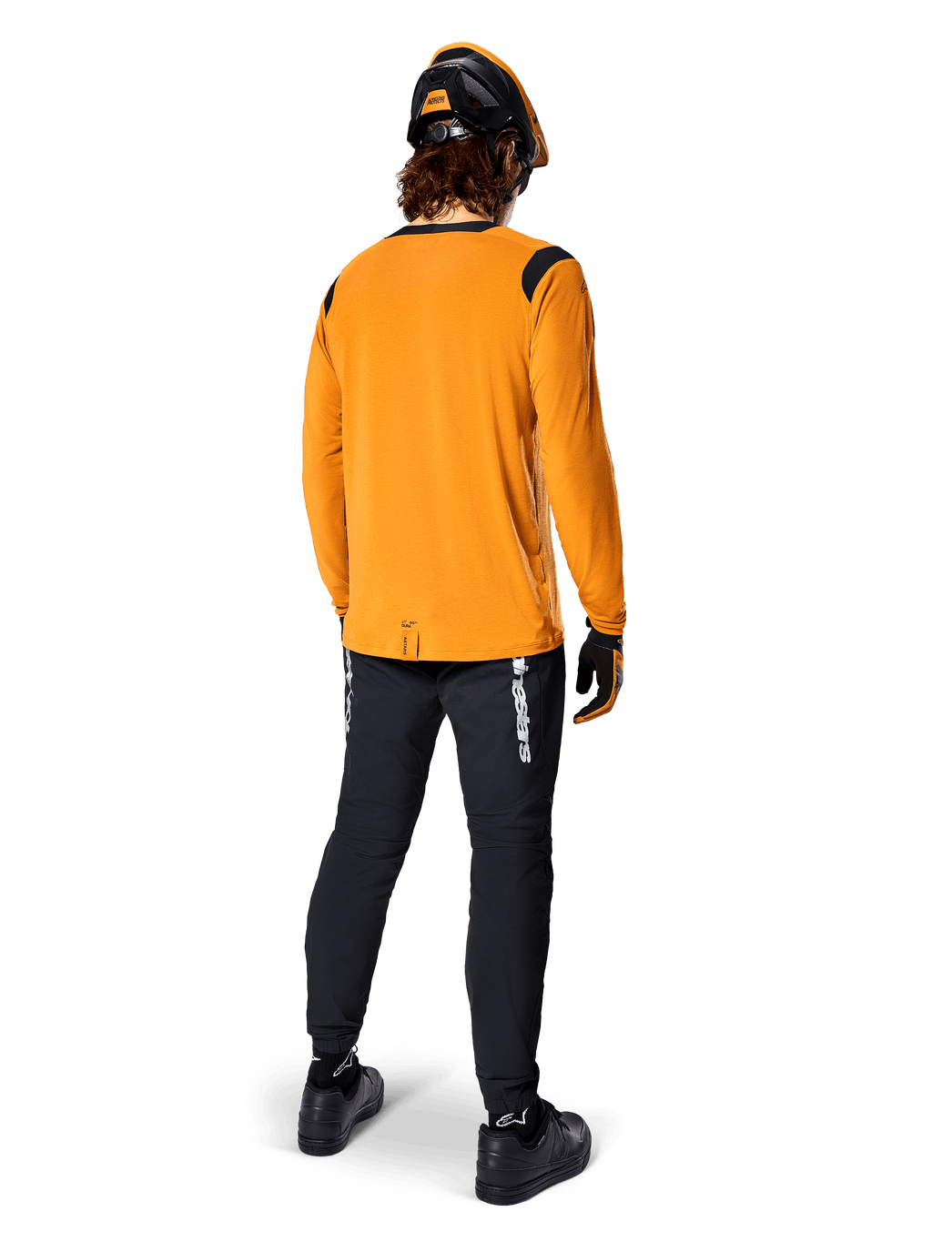 Ciclista de montanha visto de costas a usar a Camisola Alpinestars A-Dura Dri Wool de Manga Comprida em Dark Gold, calças técnicas pretas com logótipo branco e um capacete coordenado em preto e laranja, vestuário de BTT de alta performance.