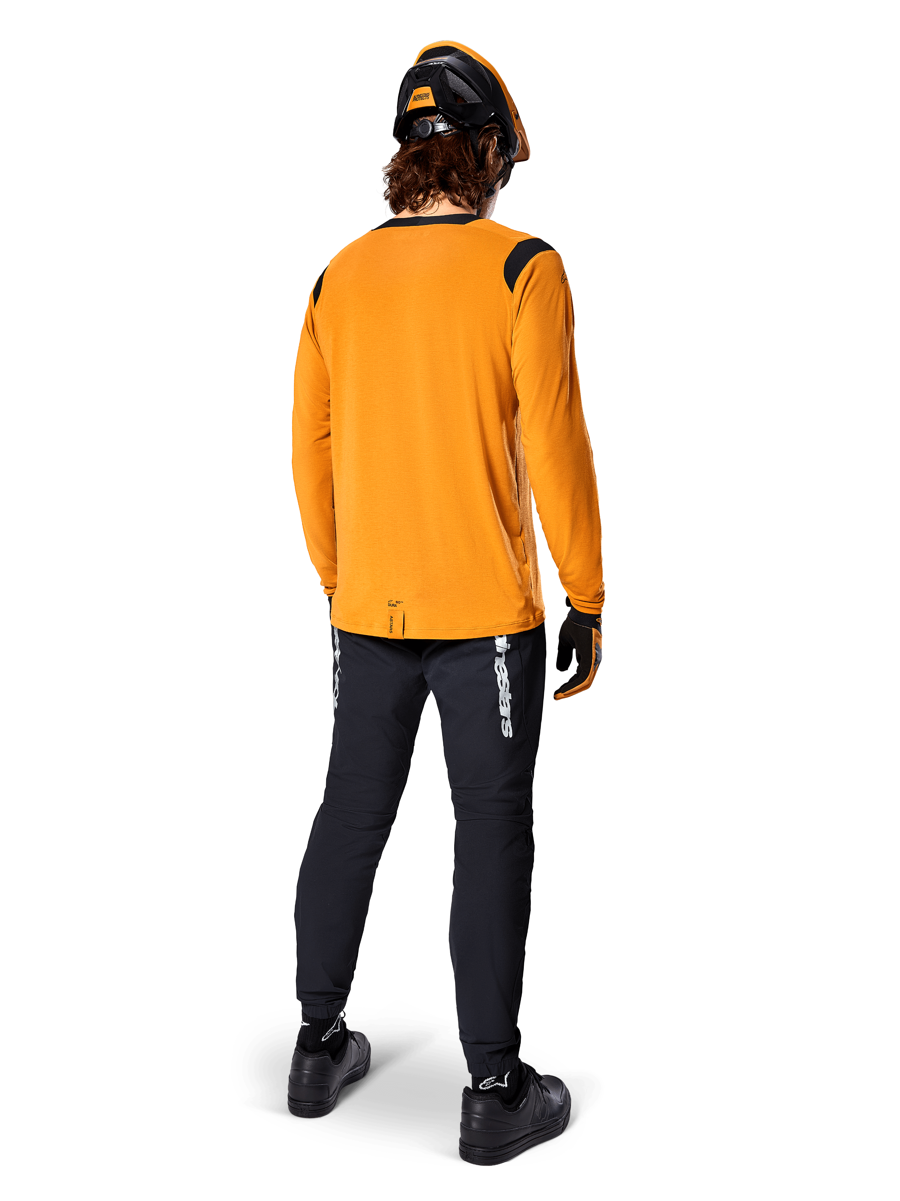 Ciclista de montanha visto de costas a usar a Camisola Alpinestars A-Dura Dri Wool de Manga Comprida em Dark Gold, calças técnicas pretas com logótipo branco e um capacete coordenado em preto e laranja, vestuário de BTT de alta performance.