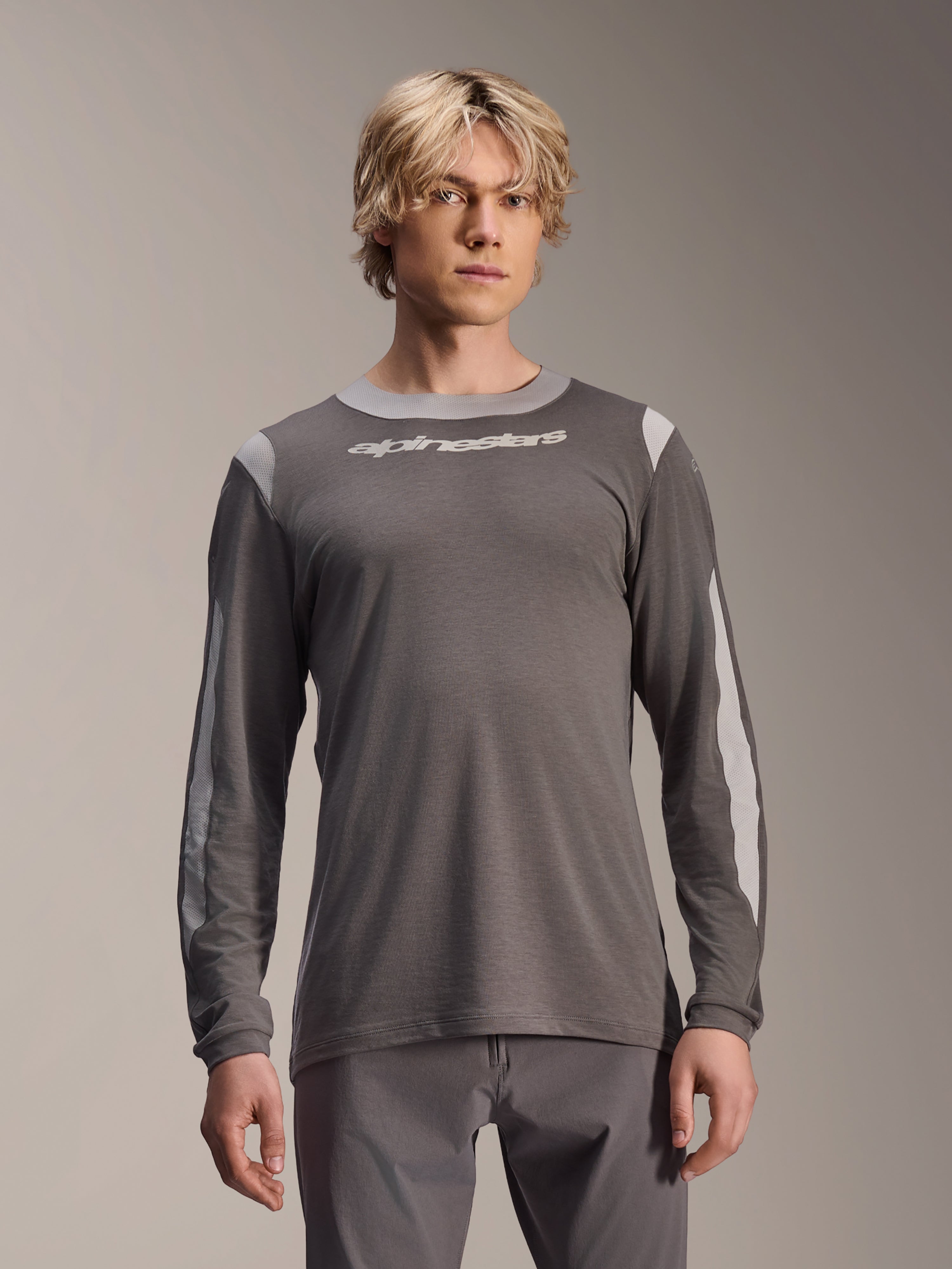 Alpinestars A-Dura Dri Wool Jersey de manga comprida, cinzento escuro, vestida por modelo masculino, com painéis de malha cinzento claro nos ombros e mangas, logótipo branco no peito, equipamento de BTT de alta performance