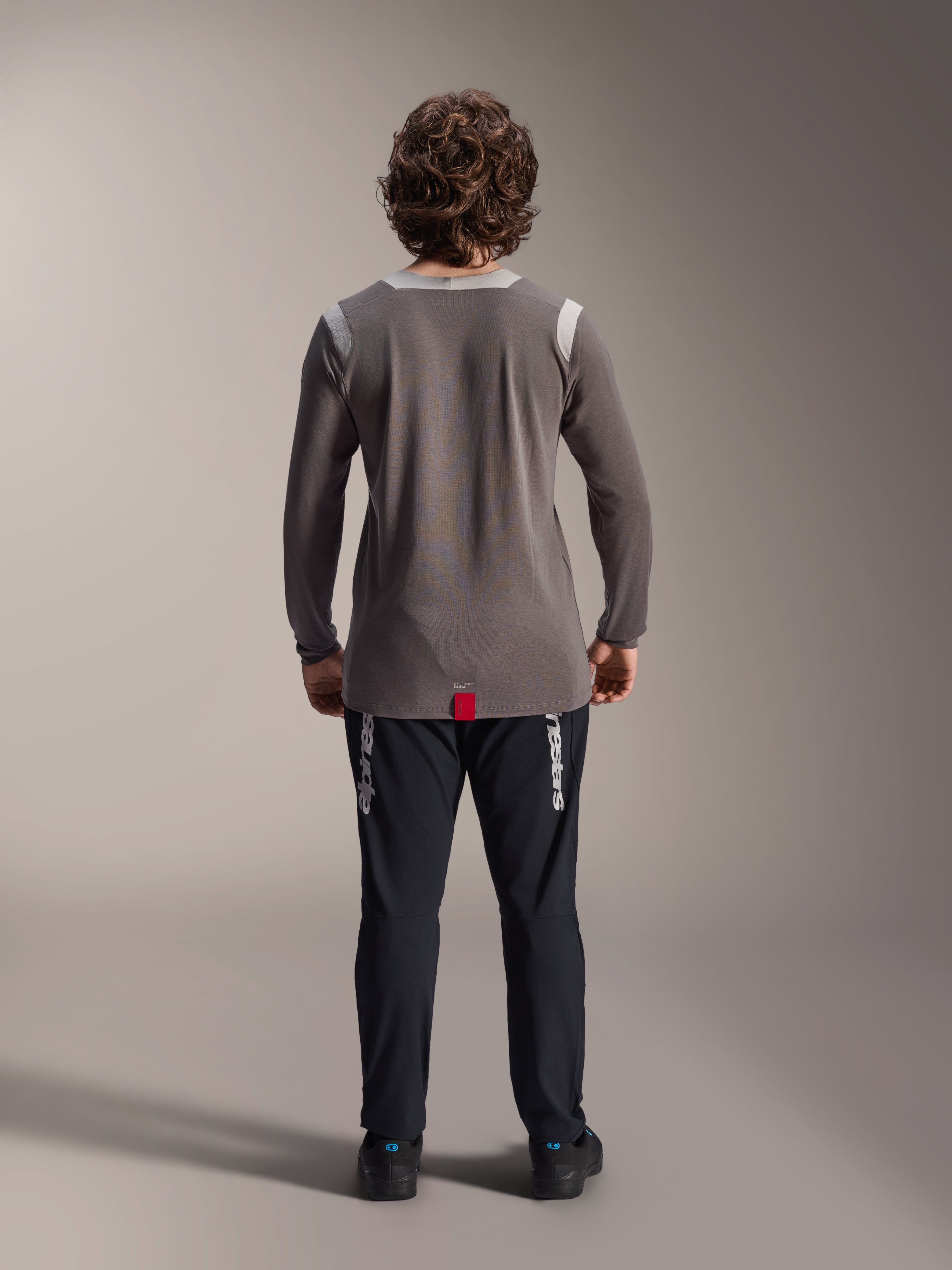 Alpinestars A-Dura Elite Pants e Jersey de Manga Comprida A-Dura Dri Wool, calças pretas com logótipo branco, jersey técnica cinzenta, vista traseira de conjunto de BTT, vestuário de ciclismo todo-o-terreno durável