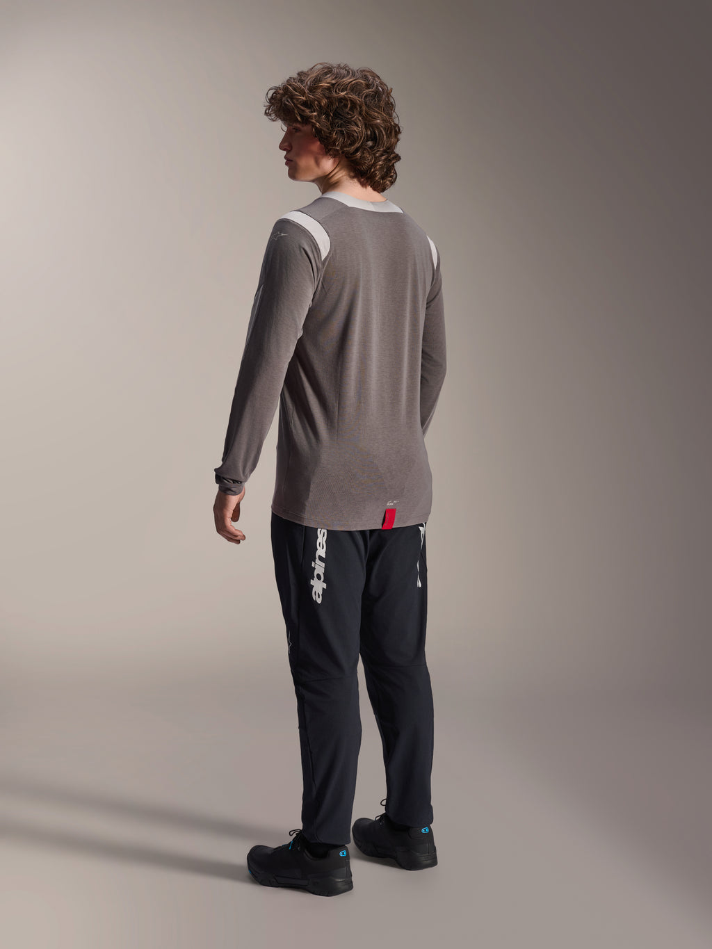 Camisola de manga comprida Alpinestars A-Dura Dri-Wool em cinzento combinada com calças A-Dura Elite em preto, vista traseira do modelo, apresentando o logótipo Alpinestars branco na perna, equipamento técnico de mountain bike para condução fora de estrada