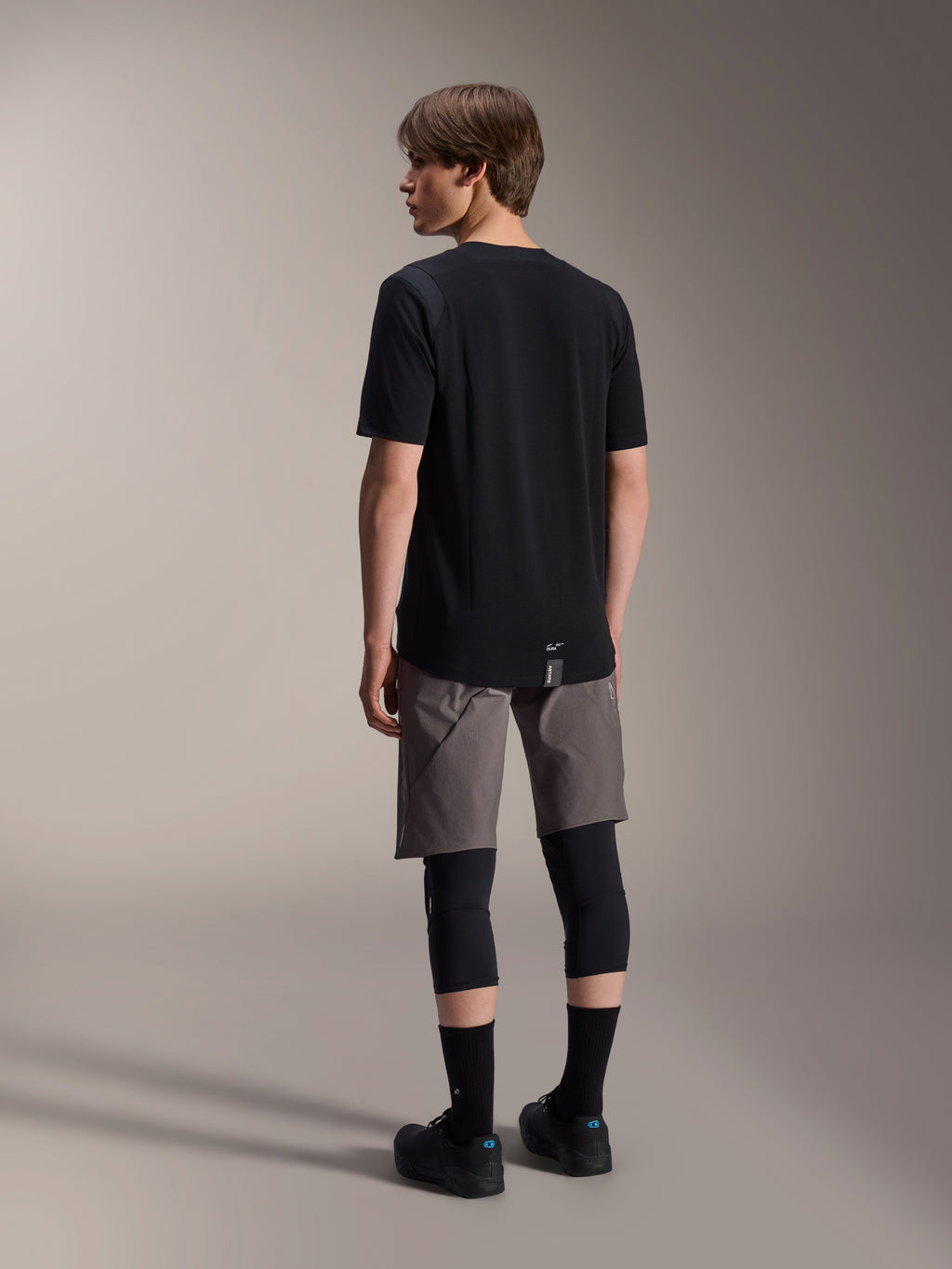 Camisola de Manga Curta Alpinestars A-Dura Dri Wool e Calções A-Dura Elite, vestuário de mountain bike em preto e cinzento escuro, com joelheiras e meias pretas, vista traseira de equipamento de ciclismo para performance fora de estrada