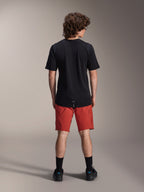 Modelo masculino a usar calções Alpinestars A-Dura Elite em Dark Orange e camisola de manga curta A-Dura Dri Wool em preto, visto de costas, combinado com meias pretas e sapatos de ciclismo, vestuário profissional de mountain bike