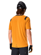 Camisola Alpinestars A-Dura Dri Wool de Manga Curta, Amarelo Escuro, vista traseira de um homem a usar a camisola com painéis de malha pretos nos ombros, combinada com capacete de BTT e luvas pretas, equipamento de ciclismo de montanha de ajuste regular