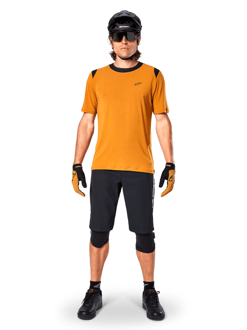 Camisola de Manga Curta Alpinestars A-Dura Dri Wool em Dark Gold, camisola de mountain bike usada com calções pretos e equipamento de proteção, tecido amarelo mostarda com gola e detalhes pretos nos ombros, vestuário de ciclismo de performance para trilhos.