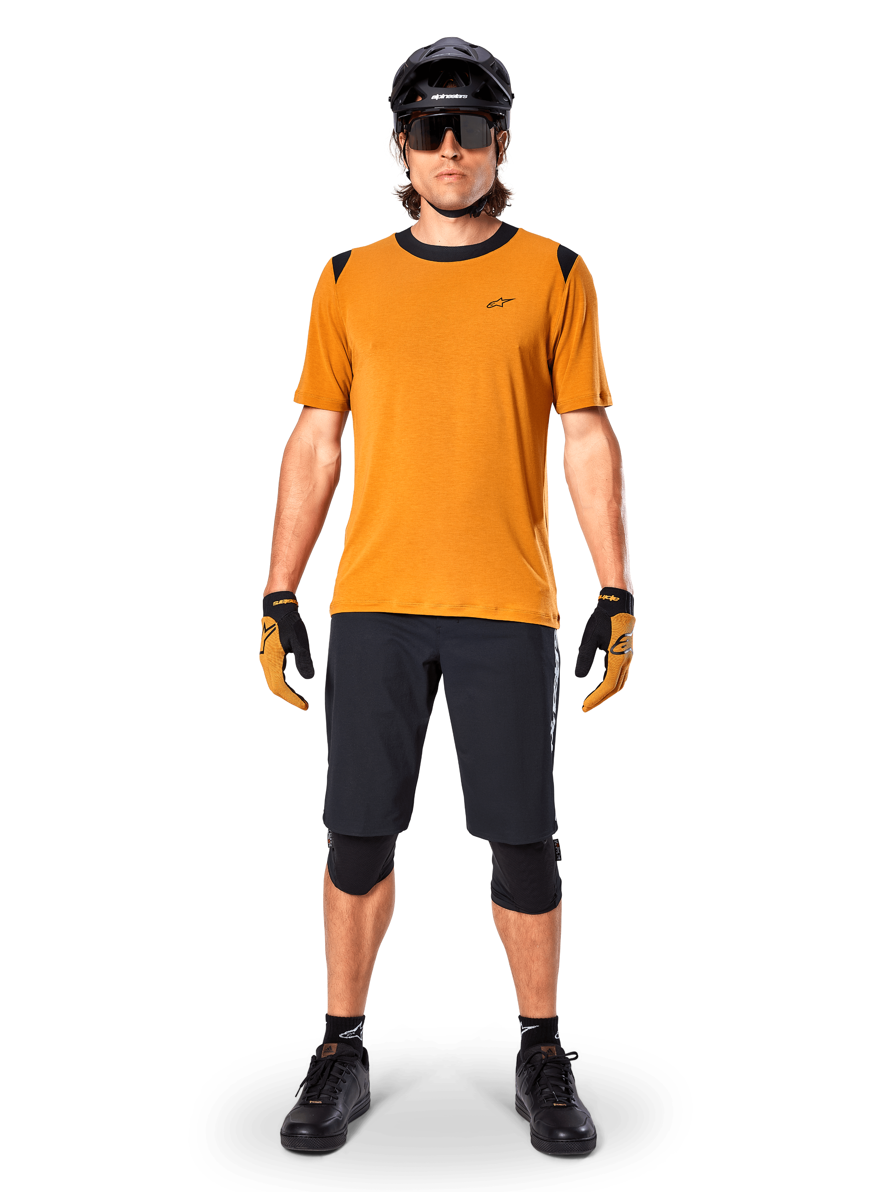 Camisola de Manga Curta Alpinestars A-Dura Dri Wool em Dark Gold, camisola de mountain bike usada com calções pretos e equipamento de proteção, tecido amarelo mostarda com gola e detalhes pretos nos ombros, vestuário de ciclismo de performance para trilhos.