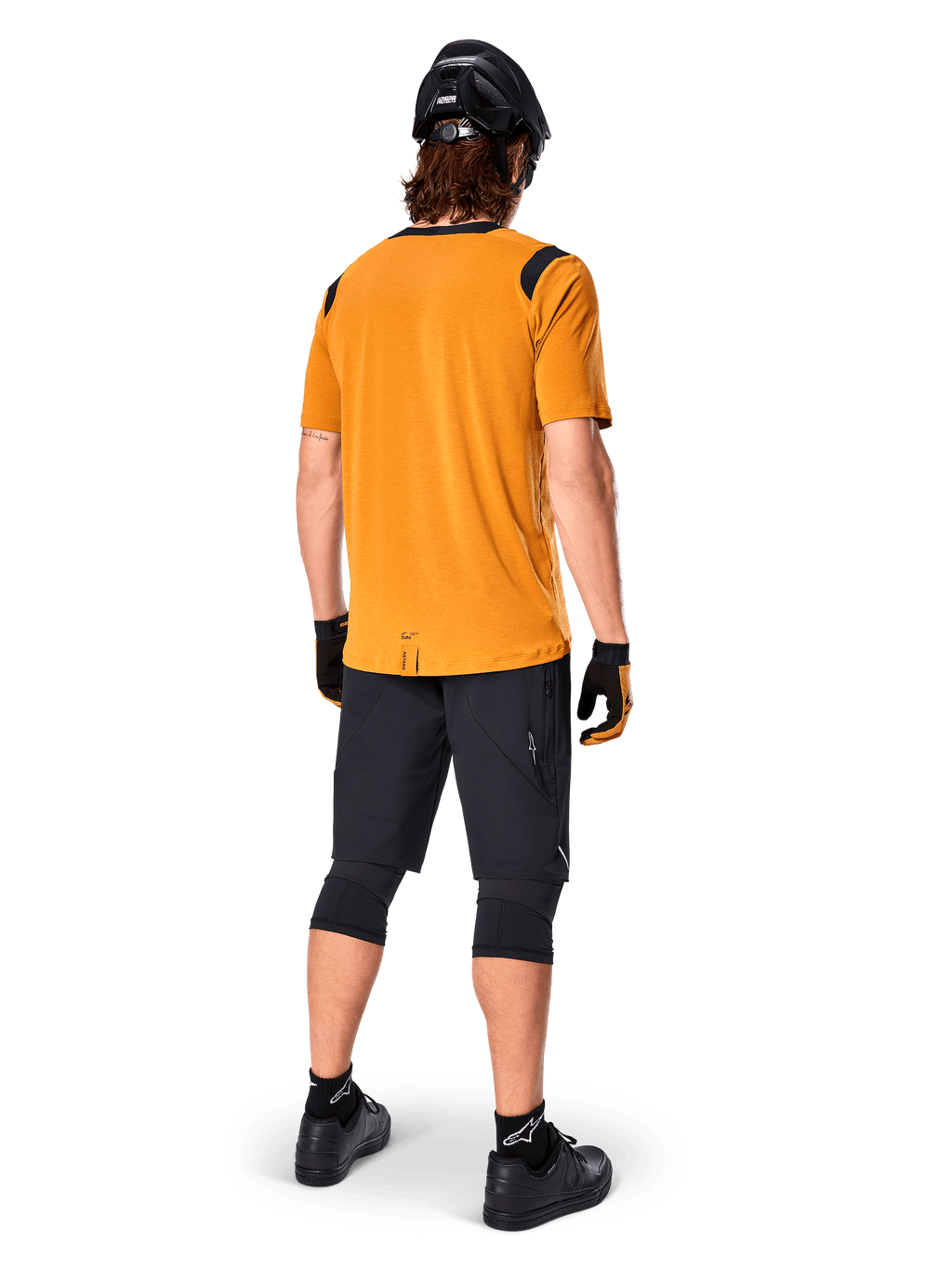Camisola de Manga Curta Alpinestars A-Dura Dri Wool, camisola de ciclismo, Dark Gold, vista traseira de ciclista de montanha com camisola amarelo-mostarda e detalhes em malha preta nos ombros, combinada com calções pretos, joelheiras, capacete preto e luvas, equipamento técnico de ciclismo todo-o-terreno
