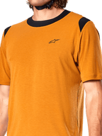 Camisola Alpinestars A-Dura Dri Wool, camisola de ciclismo de manga curta, cor dourado escuro, gola e painéis nos ombros em malha preta, pequeno logótipo preto no peito, vista frontal em grande plano