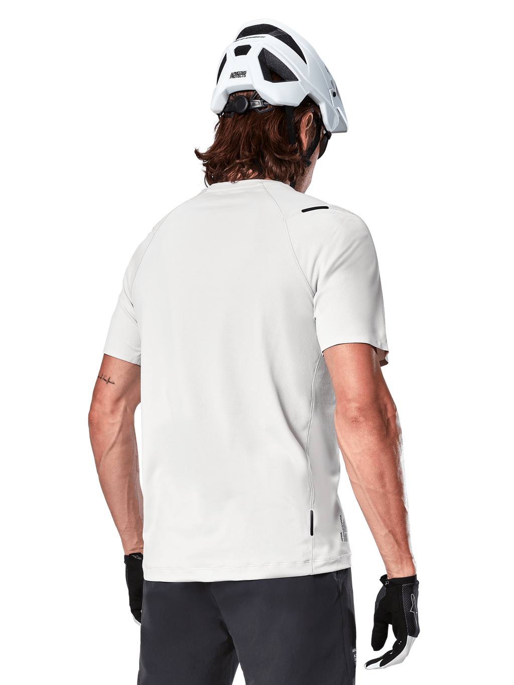 Alpinestars A-Aria Astar Jersey, Manga Curta, White Dove, vista traseira de camisola de BTT leve e respirável, usada com um capacete branco e luvas de ciclismo pretas, com cauda mais longa para maior cobertura