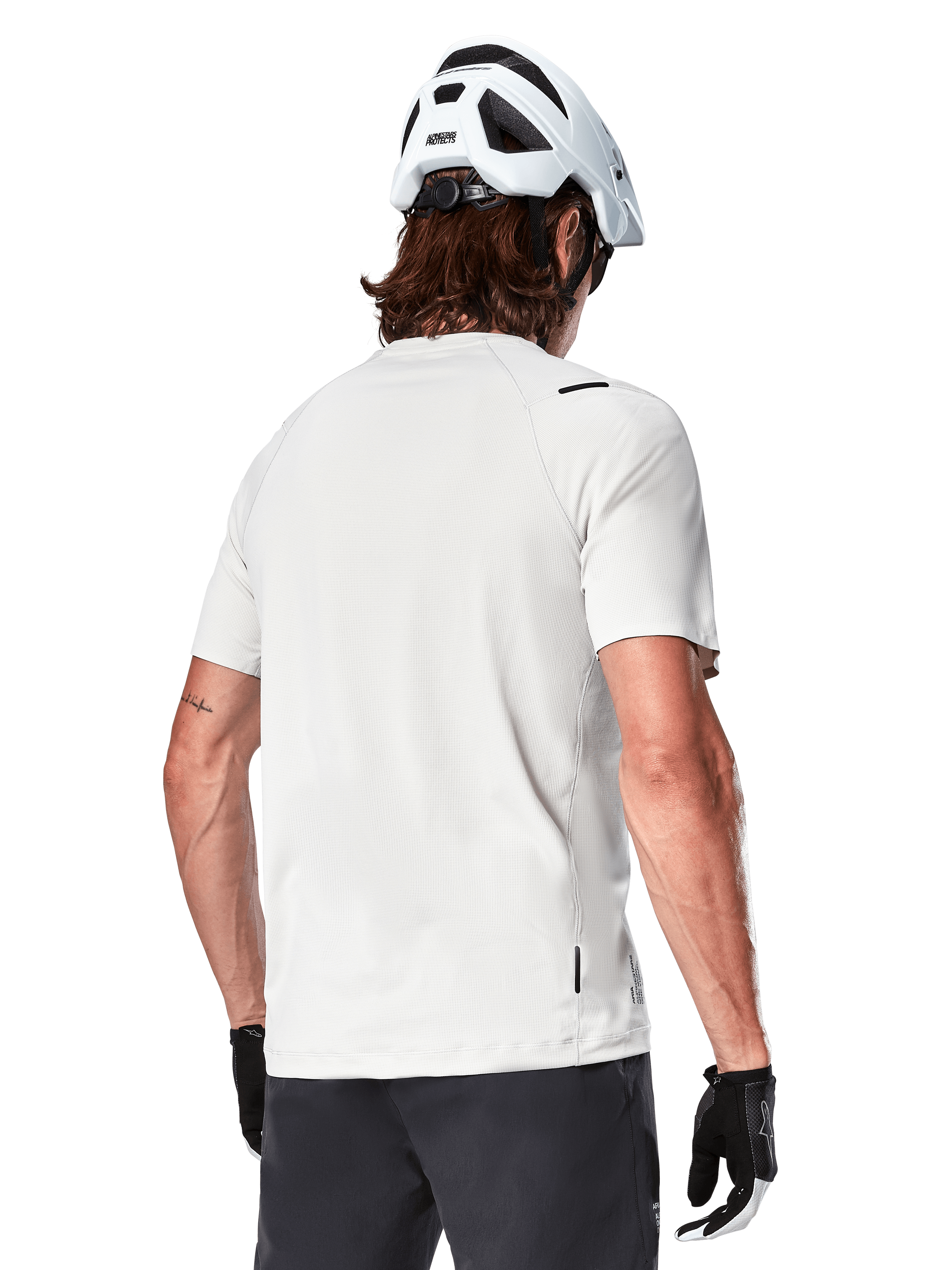 Alpinestars A-Aria Astar Jersey, Manga Curta, White Dove, vista traseira de camisola de BTT leve e respirável, usada com um capacete branco e luvas de ciclismo pretas, com cauda mais longa para maior cobertura