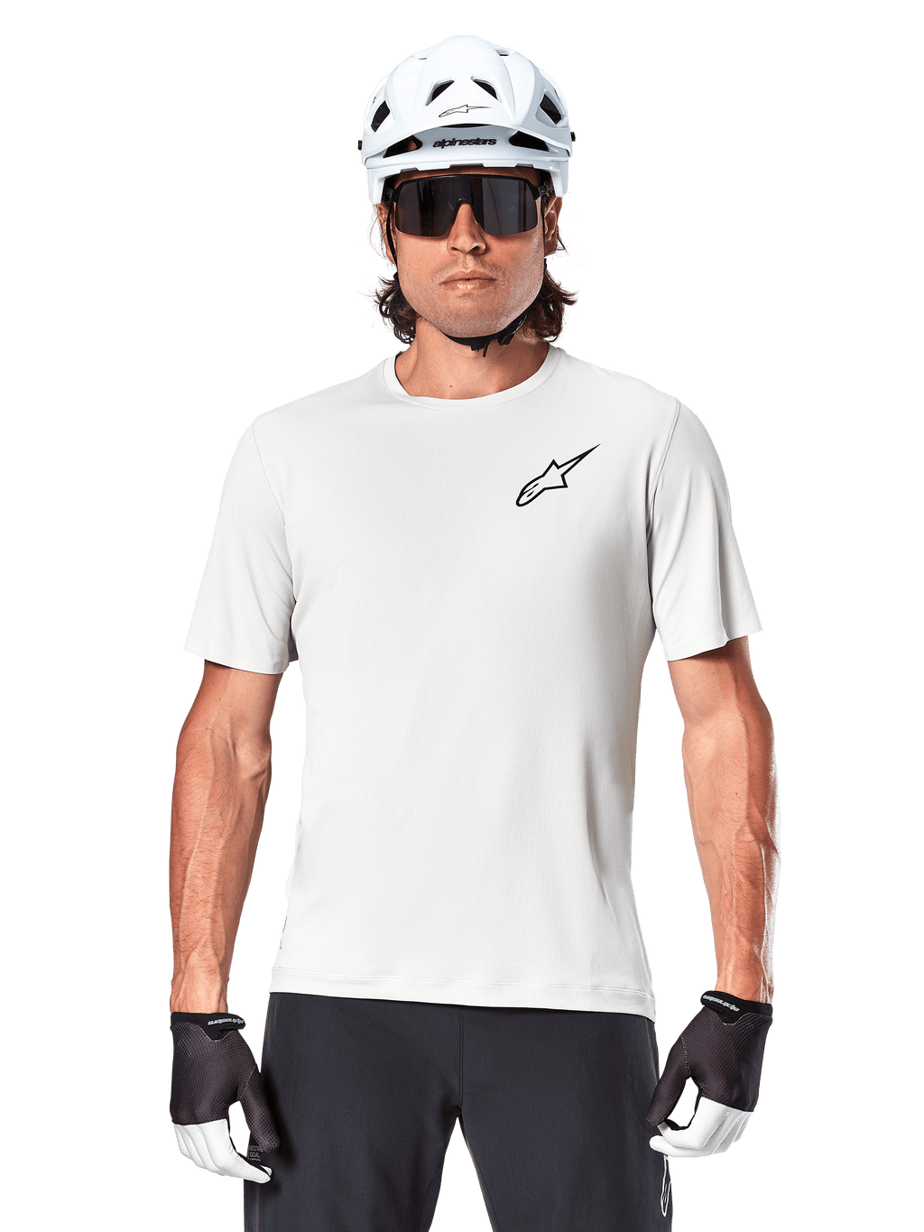 Ciclista a usar a camisola de manga curta Alpinestars A-Aria Astar, cor White Dove com um pequeno logótipo Astar preto no peito, capacete de ciclismo branco, óculos de sol pretos e luvas pretas e brancas, equipamento de performance para MTB e condução fora de estrada