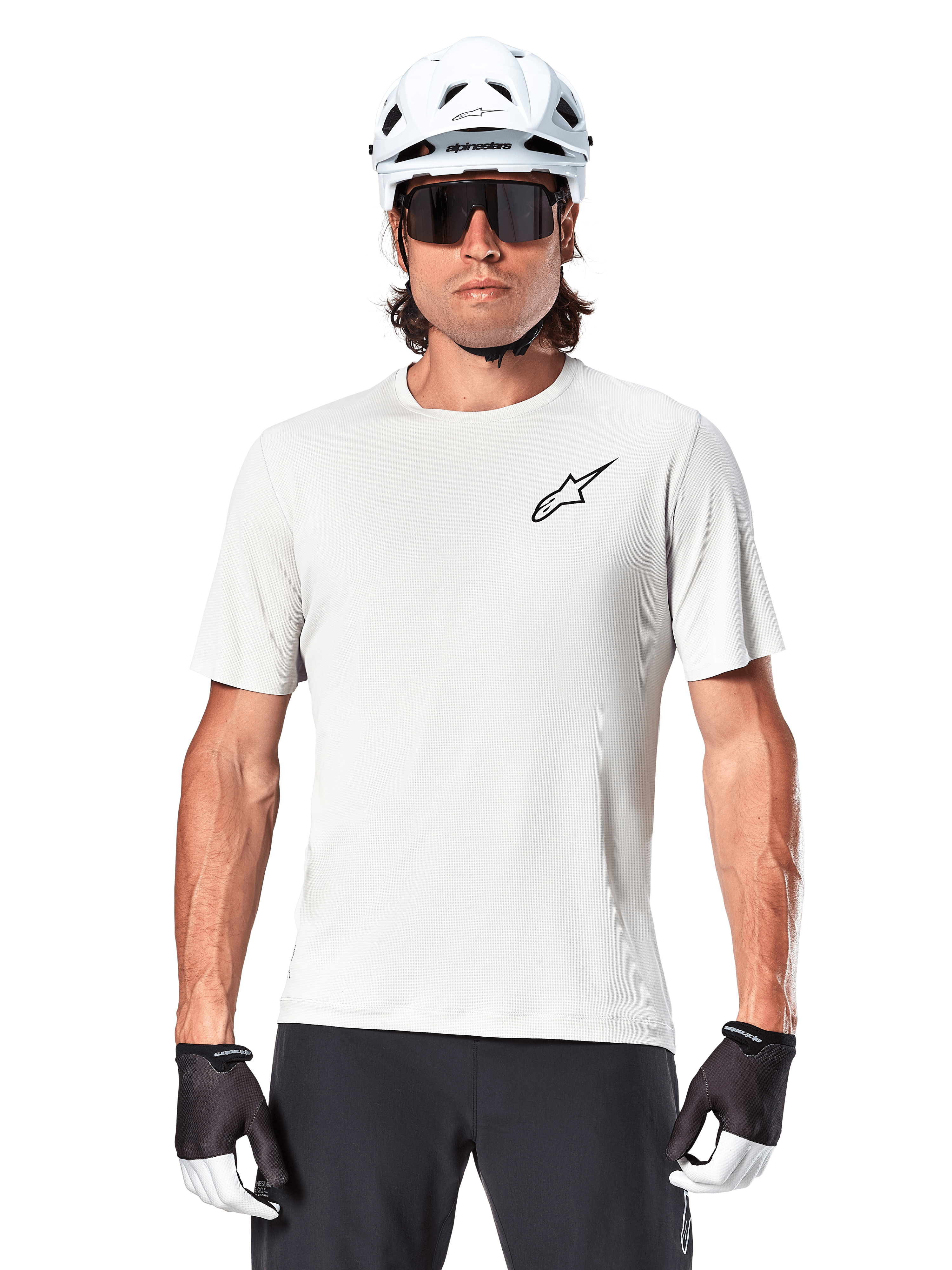 Ciclista a usar a camisola de manga curta Alpinestars A-Aria Astar, cor White Dove com um pequeno logótipo Astar preto no peito, capacete de ciclismo branco, óculos de sol pretos e luvas pretas e brancas, equipamento de performance para MTB e condução fora de estrada