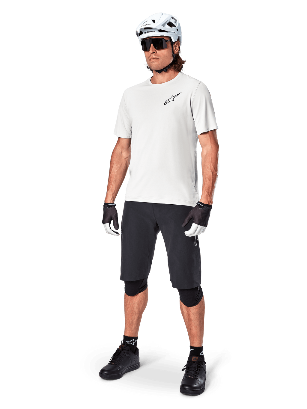 Ciclista de BTT com camisola de manga curta Alpinestars A-Aria Astar em White Dove, combinada com calções de BTT pretos, capacete branco e joelheiras pretas, com um pequeno logótipo preto no peito, equipamento de ciclismo coordenado para performance em trilhos