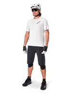 Ciclista de BTT com camisola de manga curta Alpinestars A-Aria Astar em White Dove, combinada com calções de BTT pretos, capacete branco e joelheiras pretas, com um pequeno logótipo preto no peito, equipamento de ciclismo coordenado para performance em trilhos