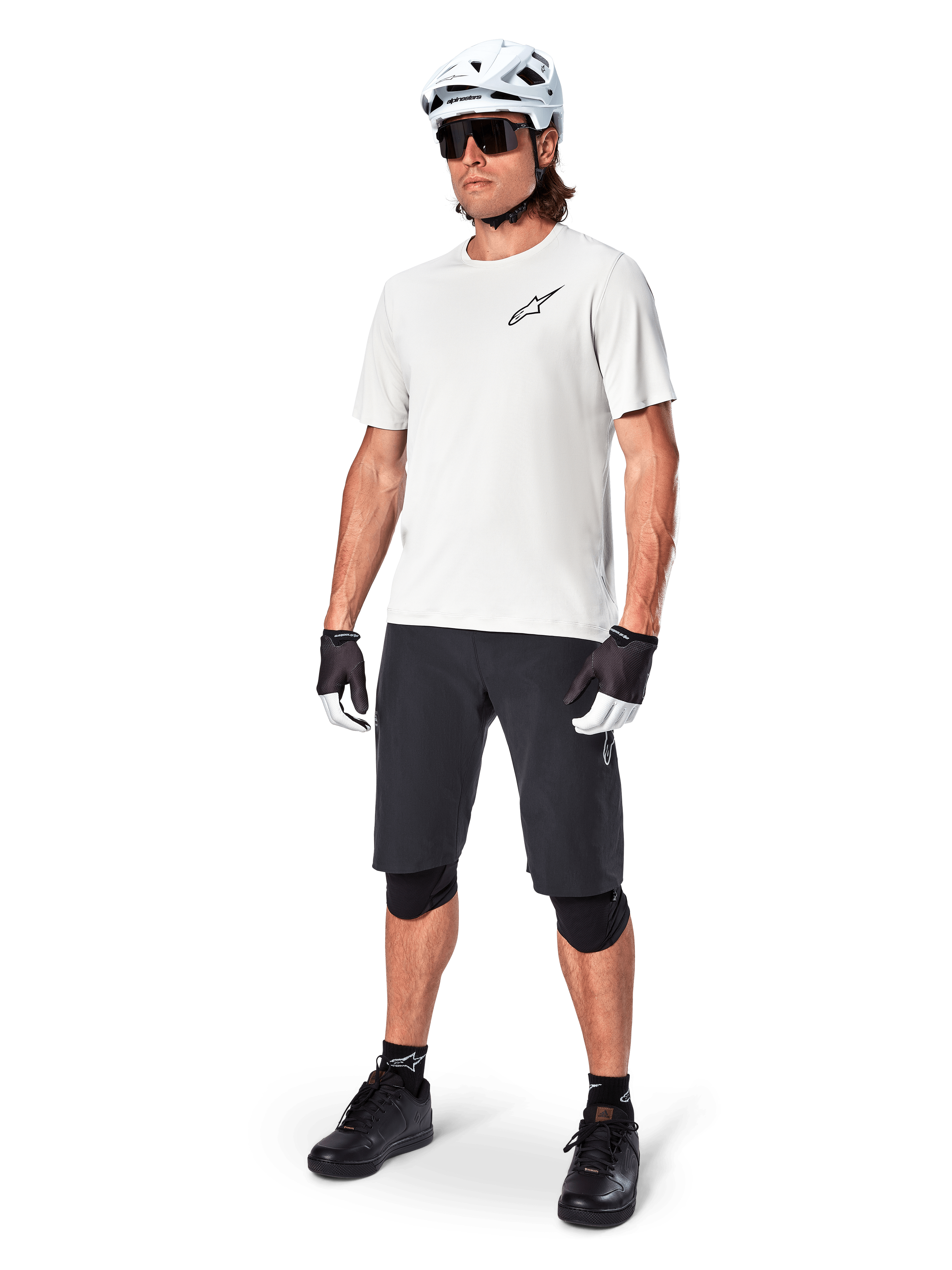 Ciclista de BTT com camisola de manga curta Alpinestars A-Aria Astar em White Dove, combinada com calções de BTT pretos, capacete branco e joelheiras pretas, com um pequeno logótipo preto no peito, equipamento de ciclismo coordenado para performance em trilhos