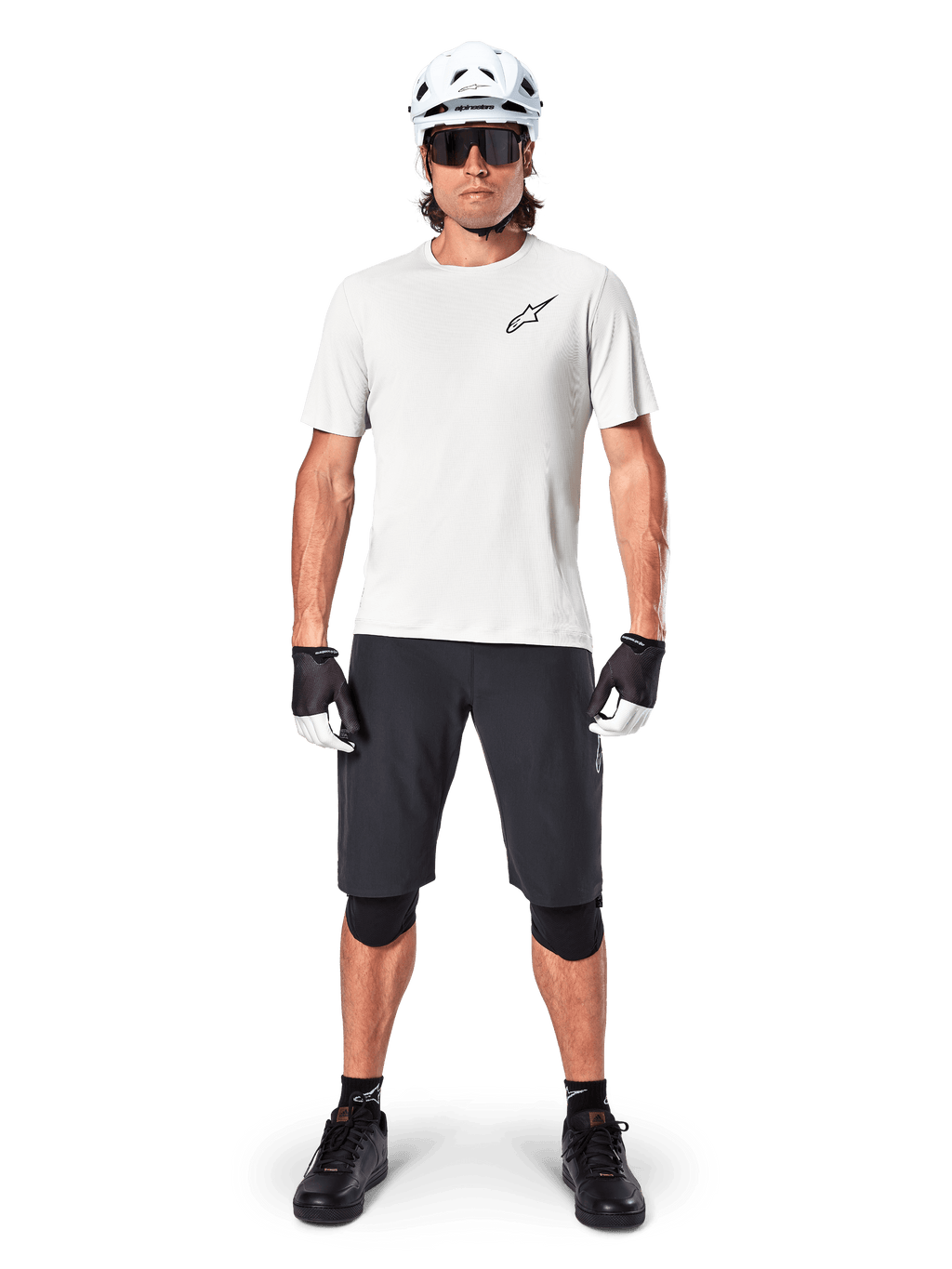 Ciclista masculino com camisola de manga curta Alpinestars A-Aria Astar em White Dove, logótipo Astars preto no peito, calções de BTT pretos, capacete branco, óculos de sol, joelheiras pretas e luvas, equipamento completo de ciclismo para todo-o-terreno