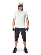 Ciclista masculino com camisola de manga curta Alpinestars A-Aria Astar em White Dove, logótipo Astars preto no peito, calções de BTT pretos, capacete branco, óculos de sol, joelheiras pretas e luvas, equipamento completo de ciclismo para todo-o-terreno