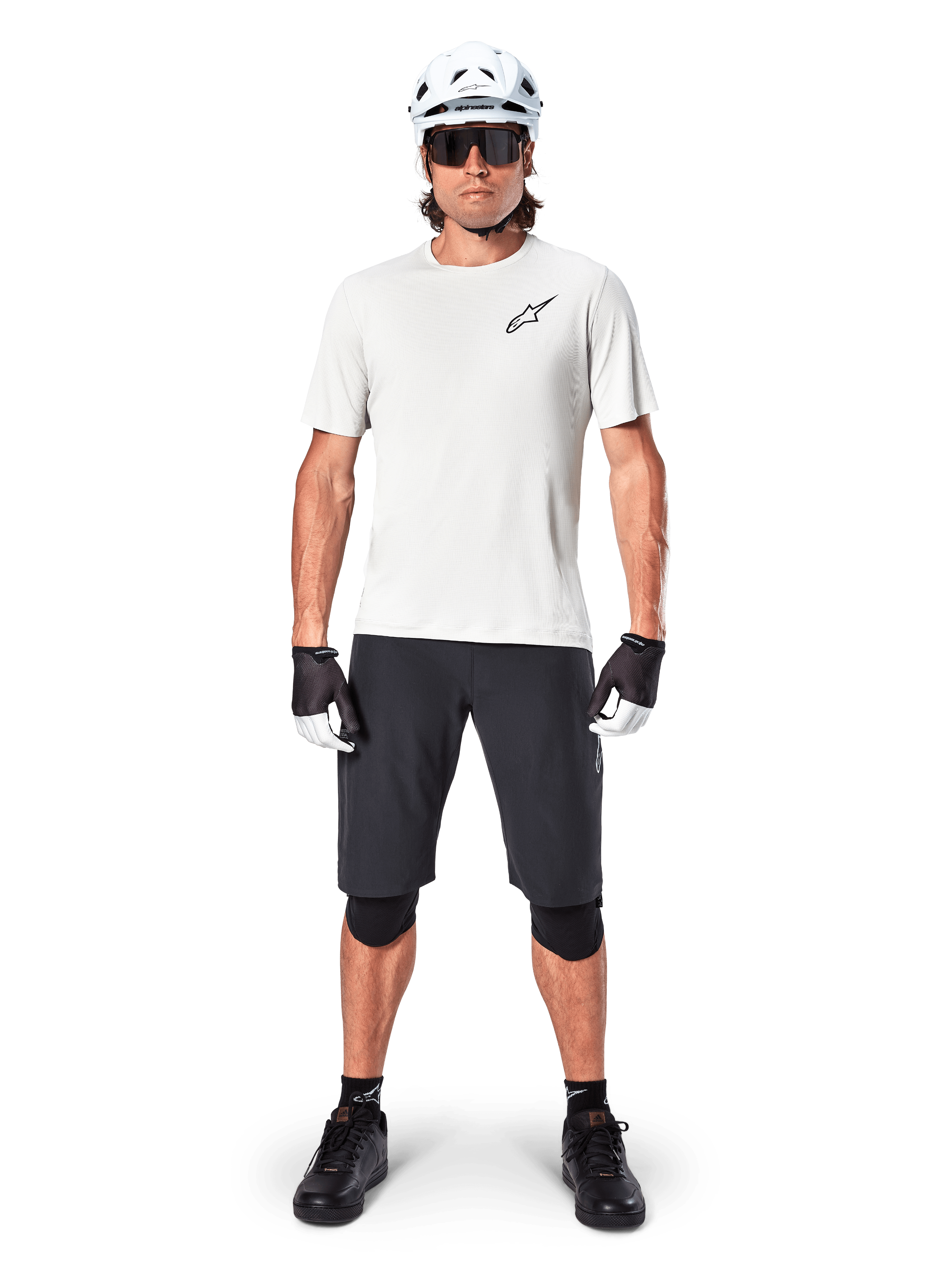 Ciclista masculino com camisola de manga curta Alpinestars A-Aria Astar em White Dove, logótipo Astars preto no peito, calções de BTT pretos, capacete branco, óculos de sol, joelheiras pretas e luvas, equipamento completo de ciclismo para todo-o-terreno