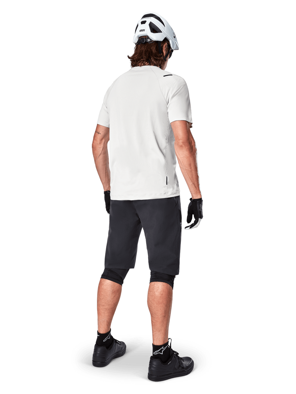 Ciclista a usar a camisola de manga curta Alpinestars A-Aria Astar em White Dove, vista traseira, combinada com calções de BTT pretos, joelheiras e um capacete branco, equipamento leve e respirável para BTT fora de estrada
