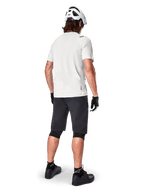 Ciclista a usar a camisola de manga curta Alpinestars A-Aria Astar em White Dove, vista traseira, combinada com calções de BTT pretos, joelheiras e um capacete branco, equipamento leve e respirável para BTT fora de estrada