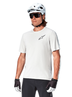 Camisola de manga curta Alpinestars A-Aria Astar, White Dove, vestida por um ciclista com capacete branco e óculos de sol escuros, com um pequeno logótipo de estrela preto no peito, equipamento de performance respirável para BTT