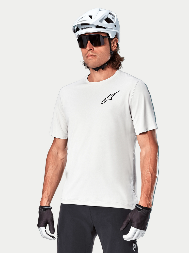 Camisola de manga curta Alpinestars A-Aria Astar, White Dove, vestida por um ciclista com capacete branco e óculos de sol escuros, com um pequeno logótipo de estrela preto no peito, equipamento de performance respirável para BTT