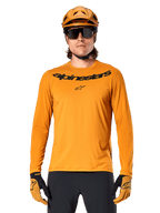 Camisola de manga comprida Alpinestars A-Dura Rocker em dourado escuro, com logótipo da marca em preto no peito, usada com capacete e luvas em dourado a condizer para performance em BTT