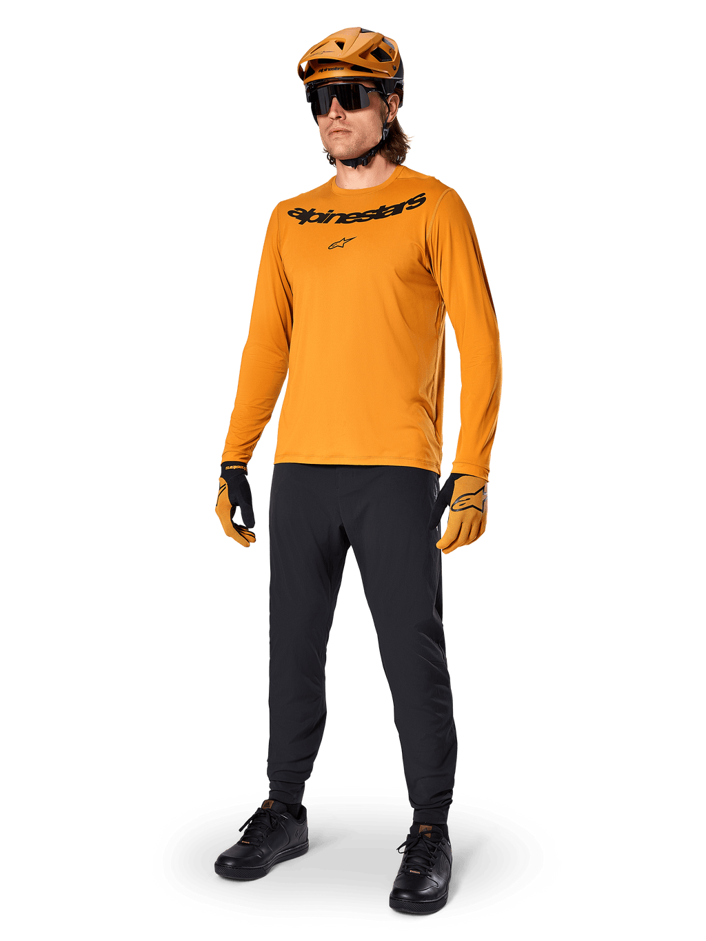 Camisola de Manga Comprida Alpinestars A-Dura Rocker, camisola de ciclismo em Dark Gold, usada com capacete de BTT a condizer e calças pretas, com logótipo da marca a preto no peito, equipamento de performance coordenado para ciclismo de montanha fora de estrada