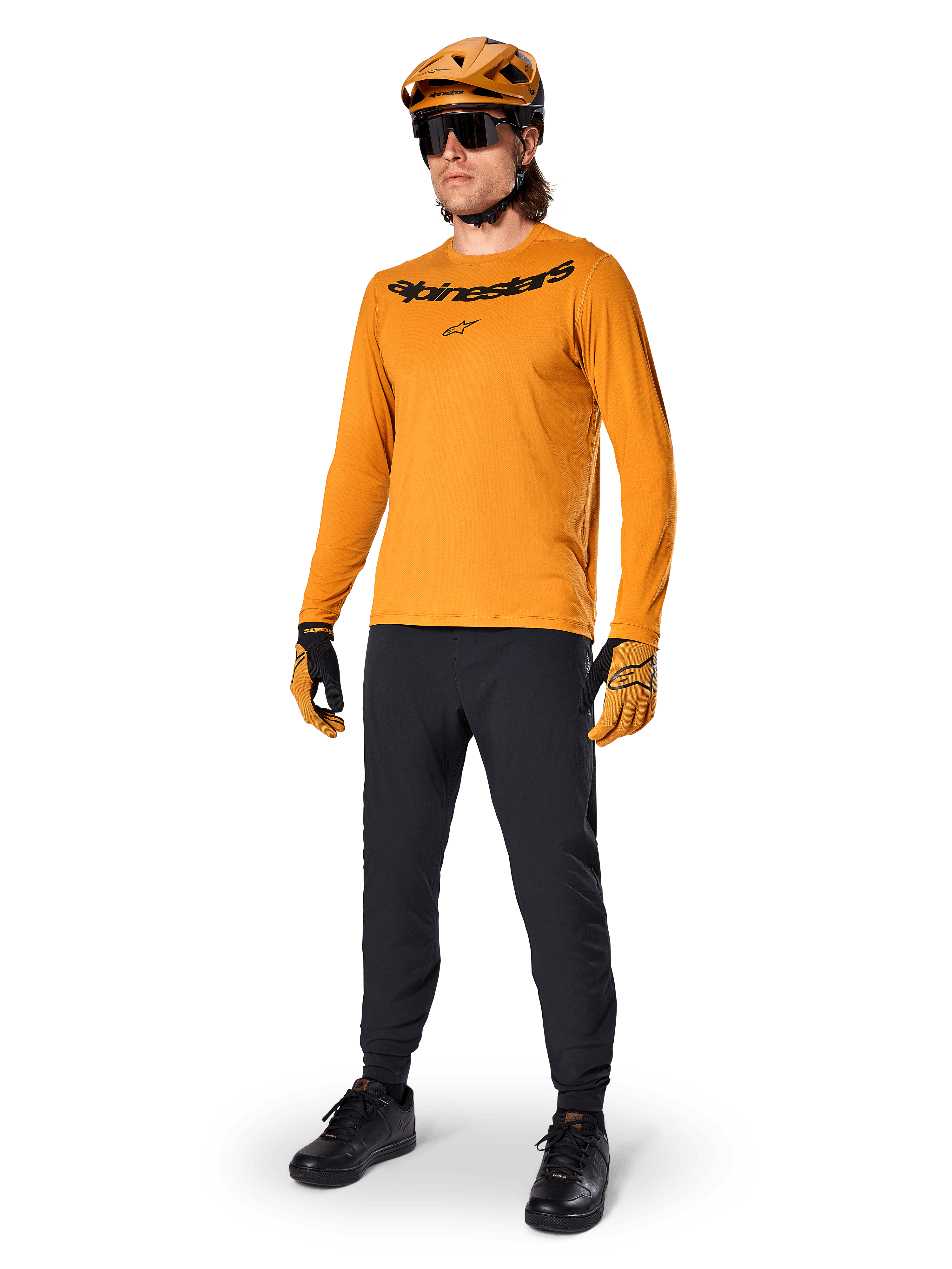 Camisola de Manga Comprida Alpinestars A-Dura Rocker, camisola de ciclismo em Dark Gold, usada com capacete de BTT a condizer e calças pretas, com logótipo da marca a preto no peito, equipamento de performance coordenado para ciclismo de montanha fora de estrada