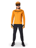 Camisola de Manga Longa Alpinestars A-Dura Rocker em Dark Gold, com logótipo preto impresso no peito, usada com um capacete de BTT dourado a condizer, óculos de sol pretos e calças pretas, equipamento profissional de mountain bike